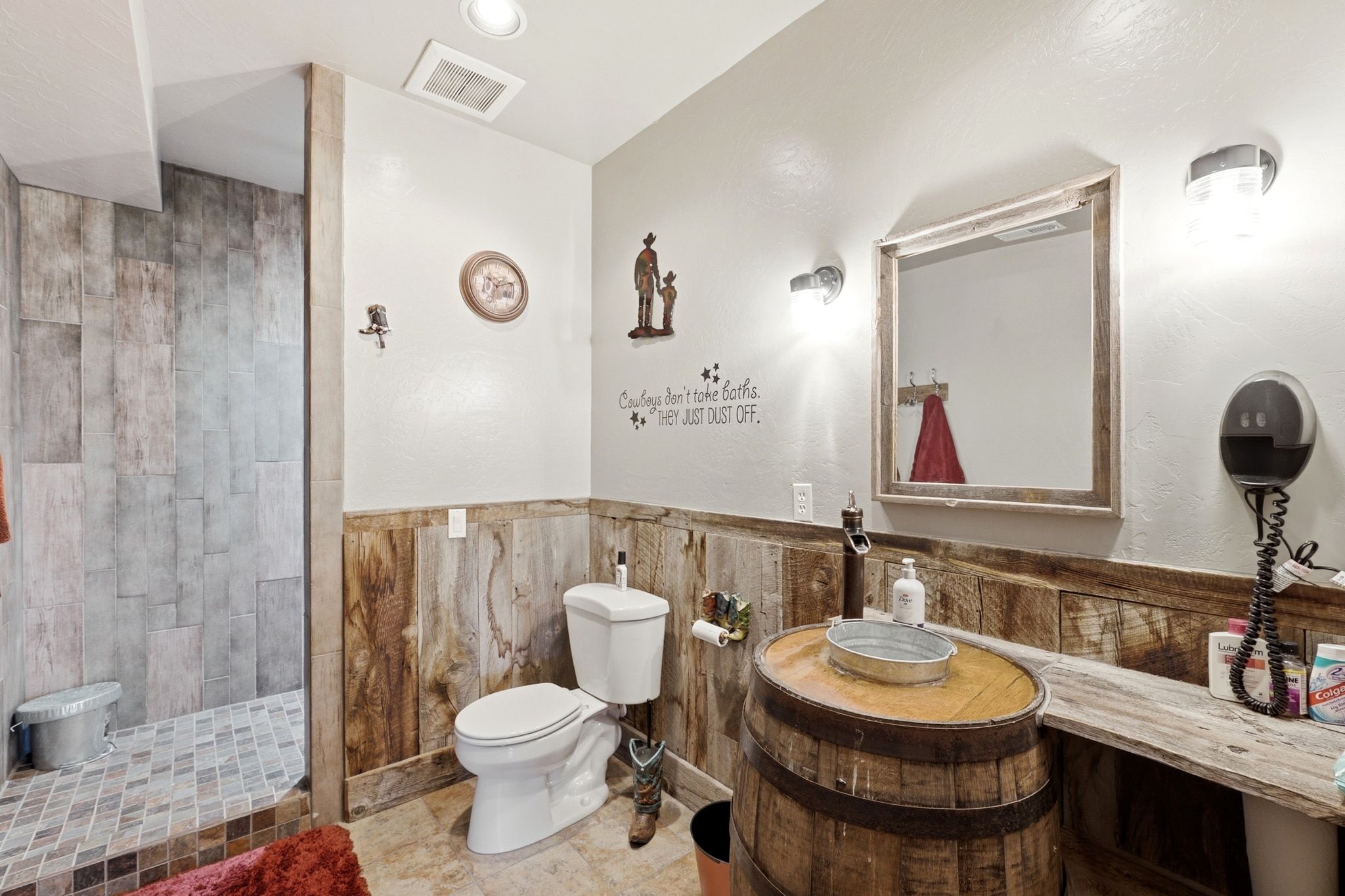 Bathroom featuring a shower with tile-finish walls and floor, a toilet, a rustic wood vanity with a basin sink, wood-finish wainscoting, and a wood-framed mirror