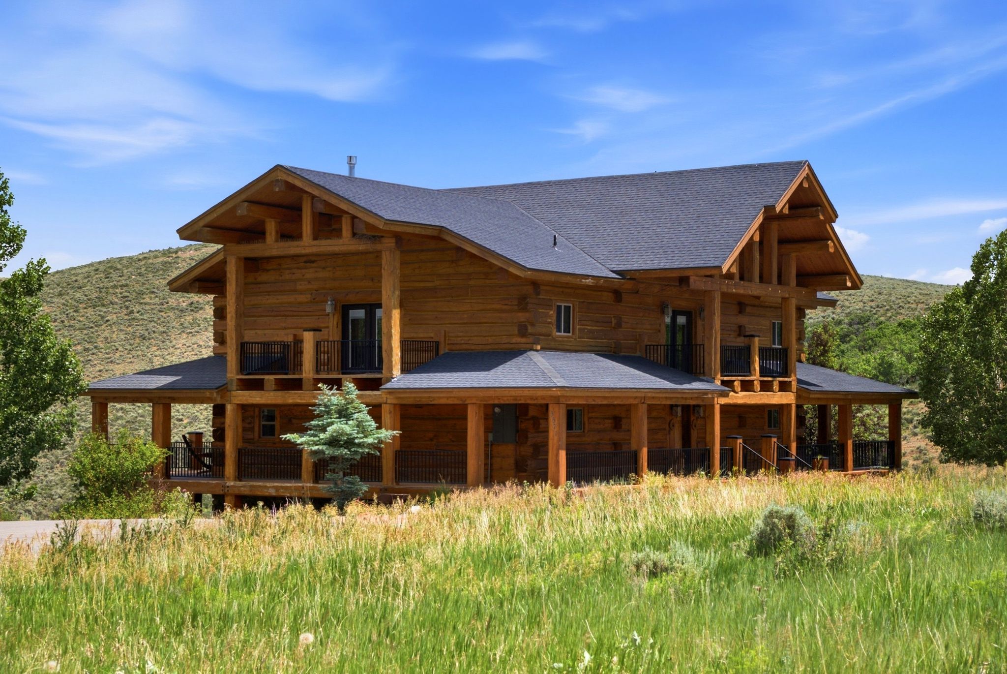 Log home exterior featuring a dark asphalt shingle roof and a wrap-around porch