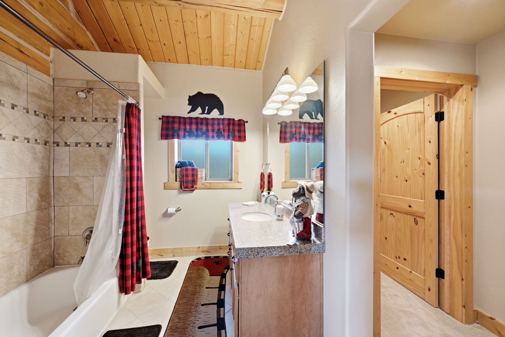 Bathroom featuring a wood-plank ceiling, tiled shower surround, integrated bathtub, wood vanity with a light-toned countertop, and an arched wood door