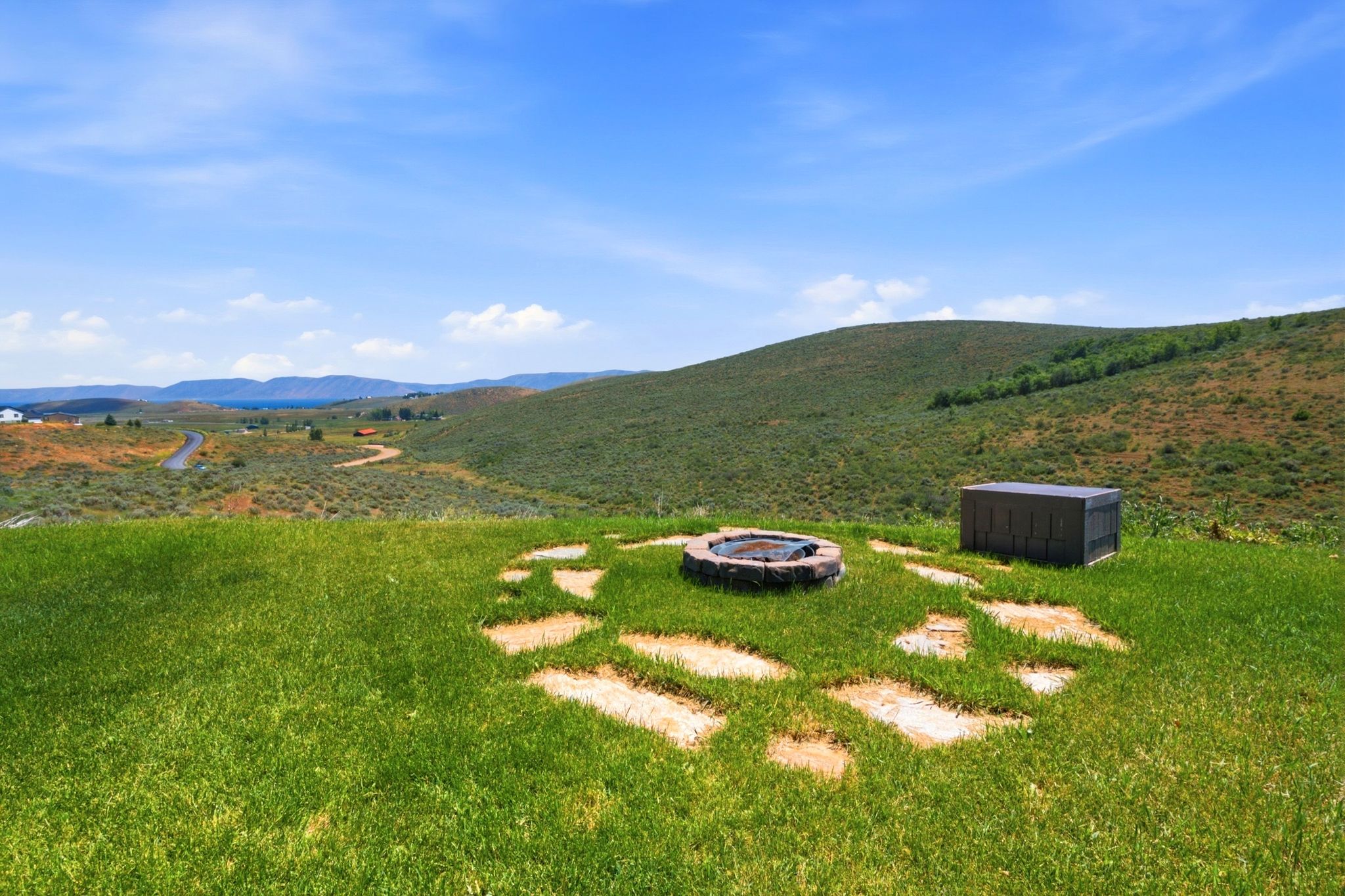 Expansive outdoor space featuring a stone fire pit, irregular stone pathway, and a utility enclosure