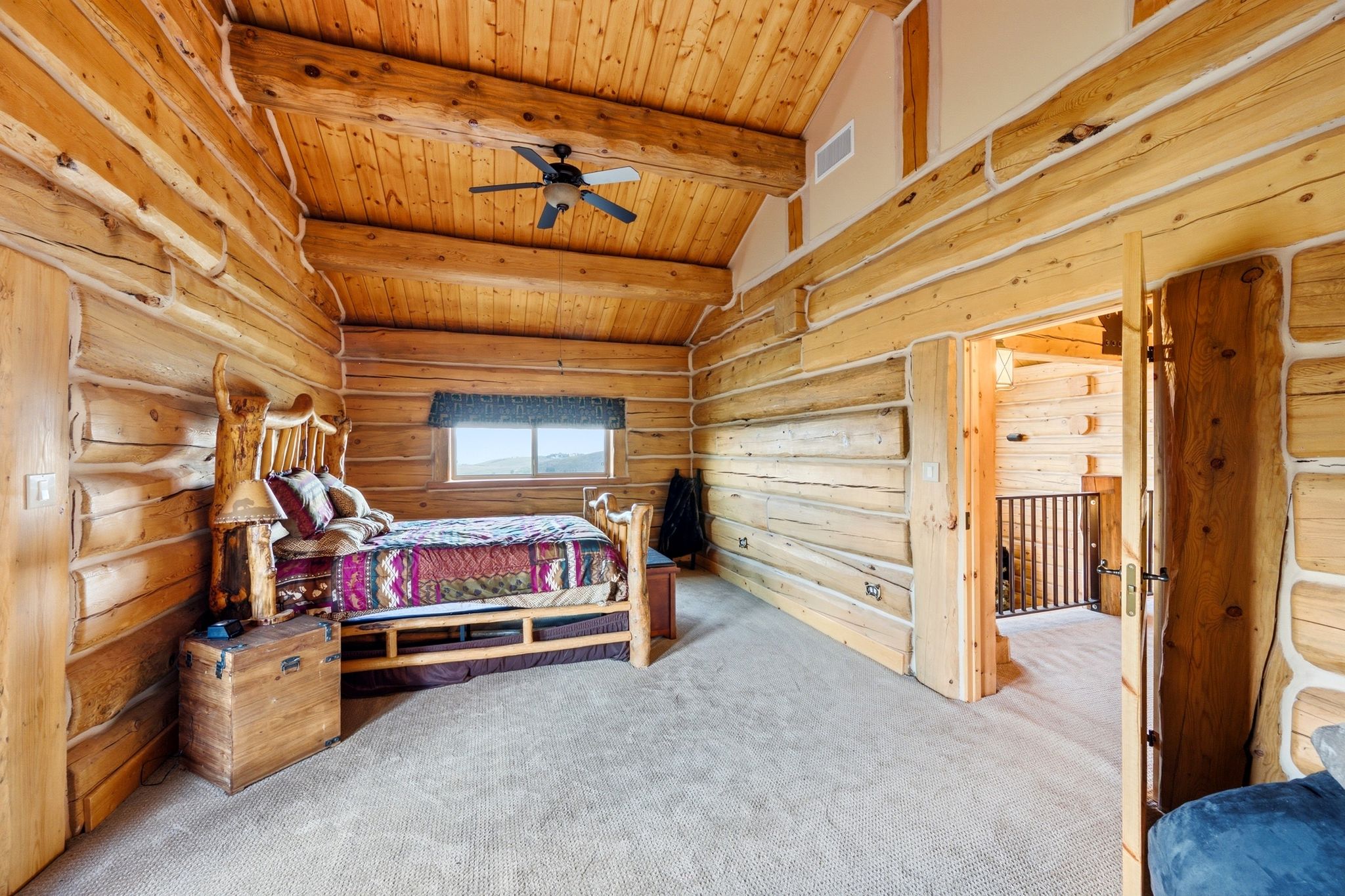 Log-style room featuring exposed wood beams, wood paneling, wood-finish flooring, a ceiling fan, and a window providing scenery