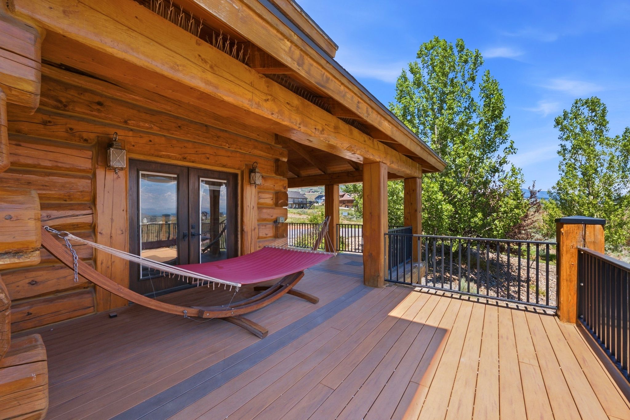 Spacious outdoor deck featuring natural wood-finish flooring, sturdy log construction, durable metal railings, an overhang for shade, and double glass doors