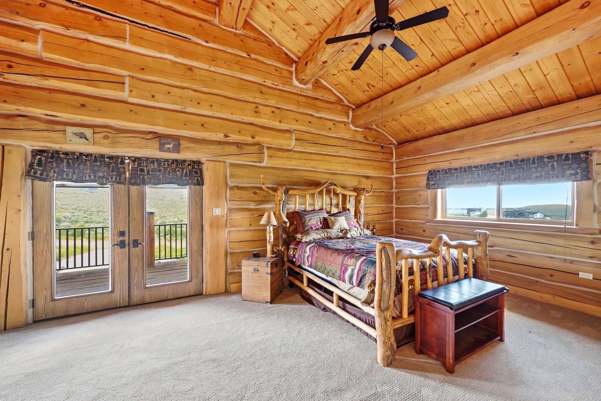 Log-style interior featuring a vaulted wood-plank ceiling with exposed beams, light-toned log walls, a ceiling fan, and light-colored carpeting