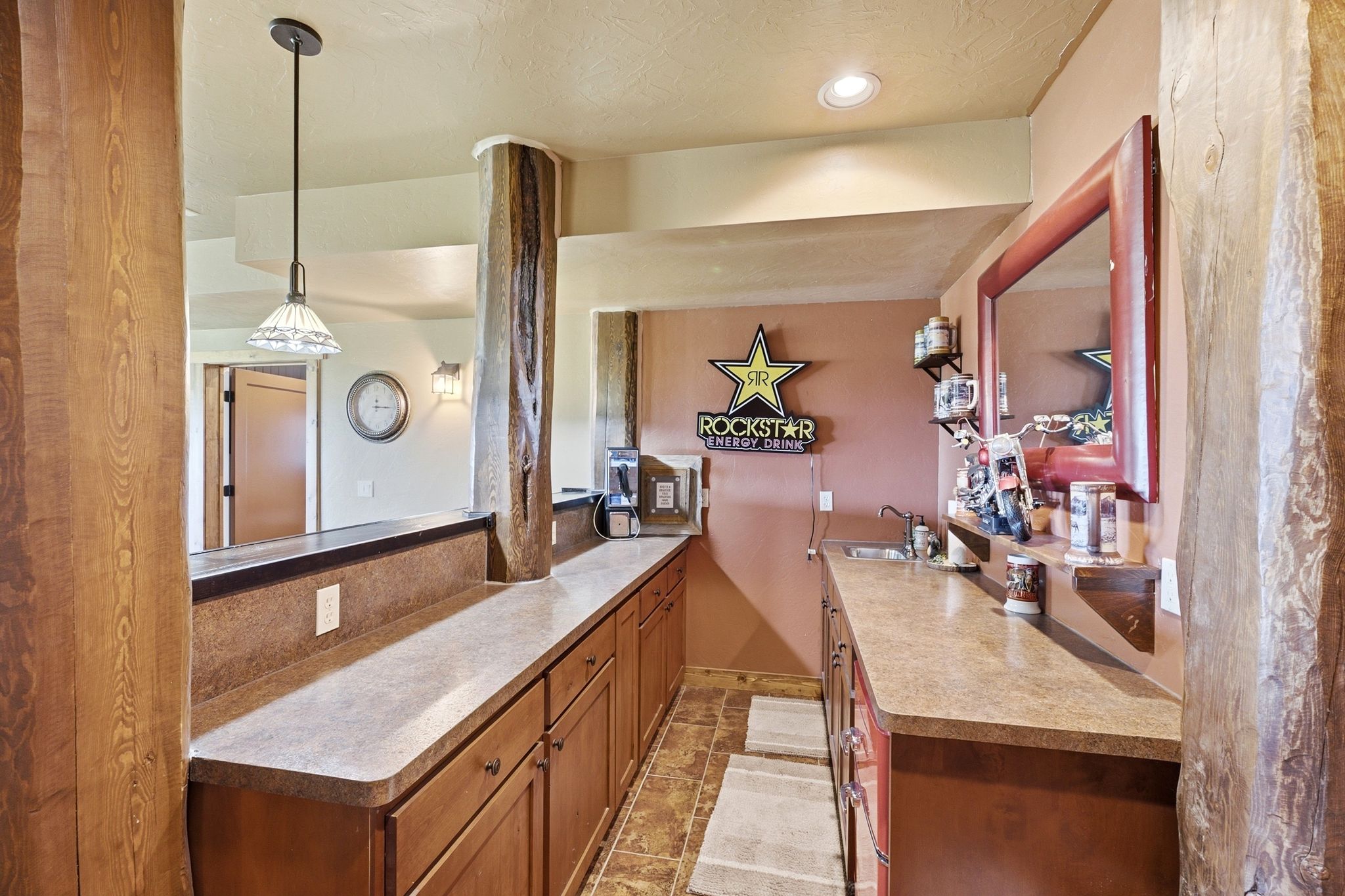 Wet bar featuring a stainless steel sink, wood cabinetry, and a light-toned countertop
