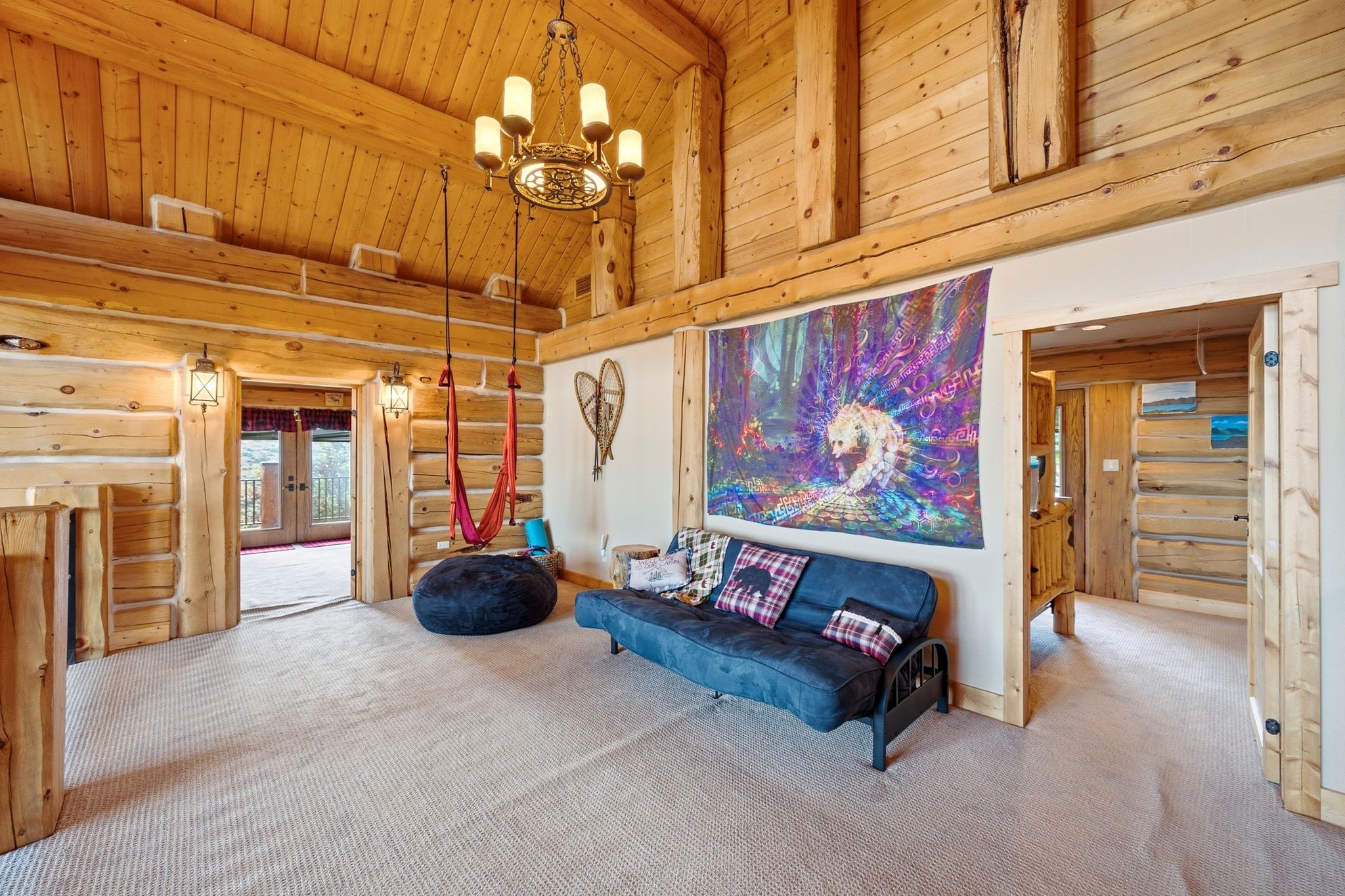 Vaulted log beam ceilings featuring a central chandelier, tongue-and-groove wood paneling, and wall-mounted sconces