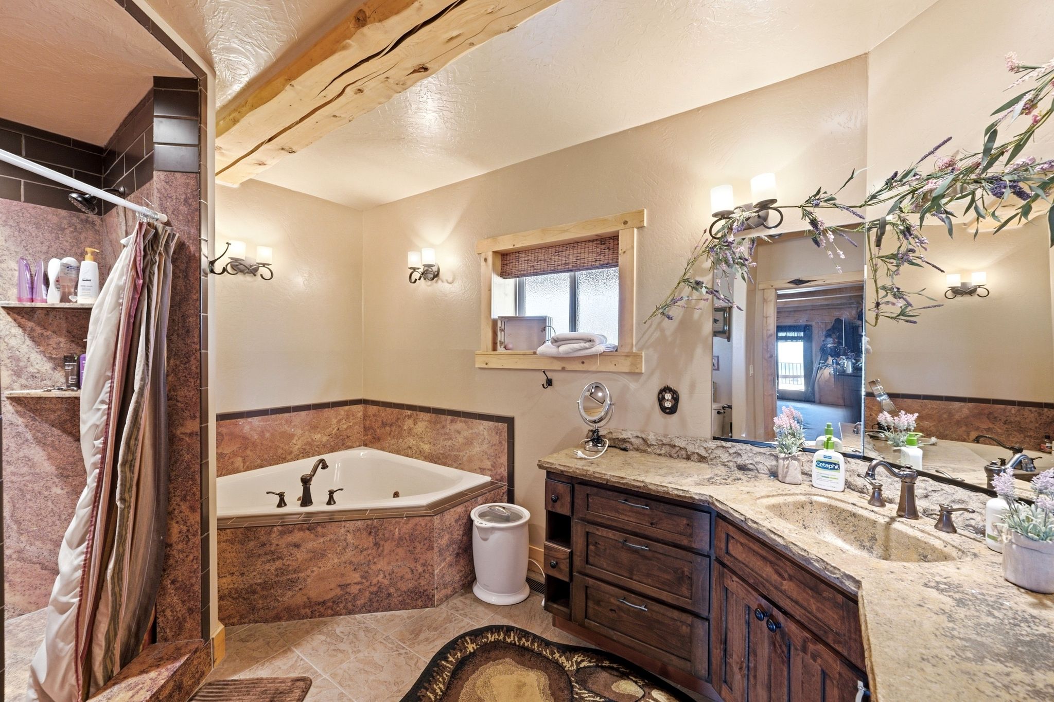 Bathroom featuring a corner jetted tub, a tiled shower with built-in shelving, a double vanity with an integrated sink and wood cabinetry, and exposed ceiling beams