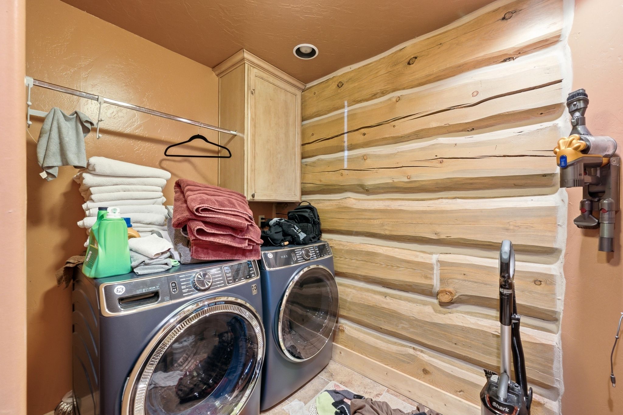 Laundry area featuring natural log wall accents, built-in cabinetry, and a chrome hanging rod