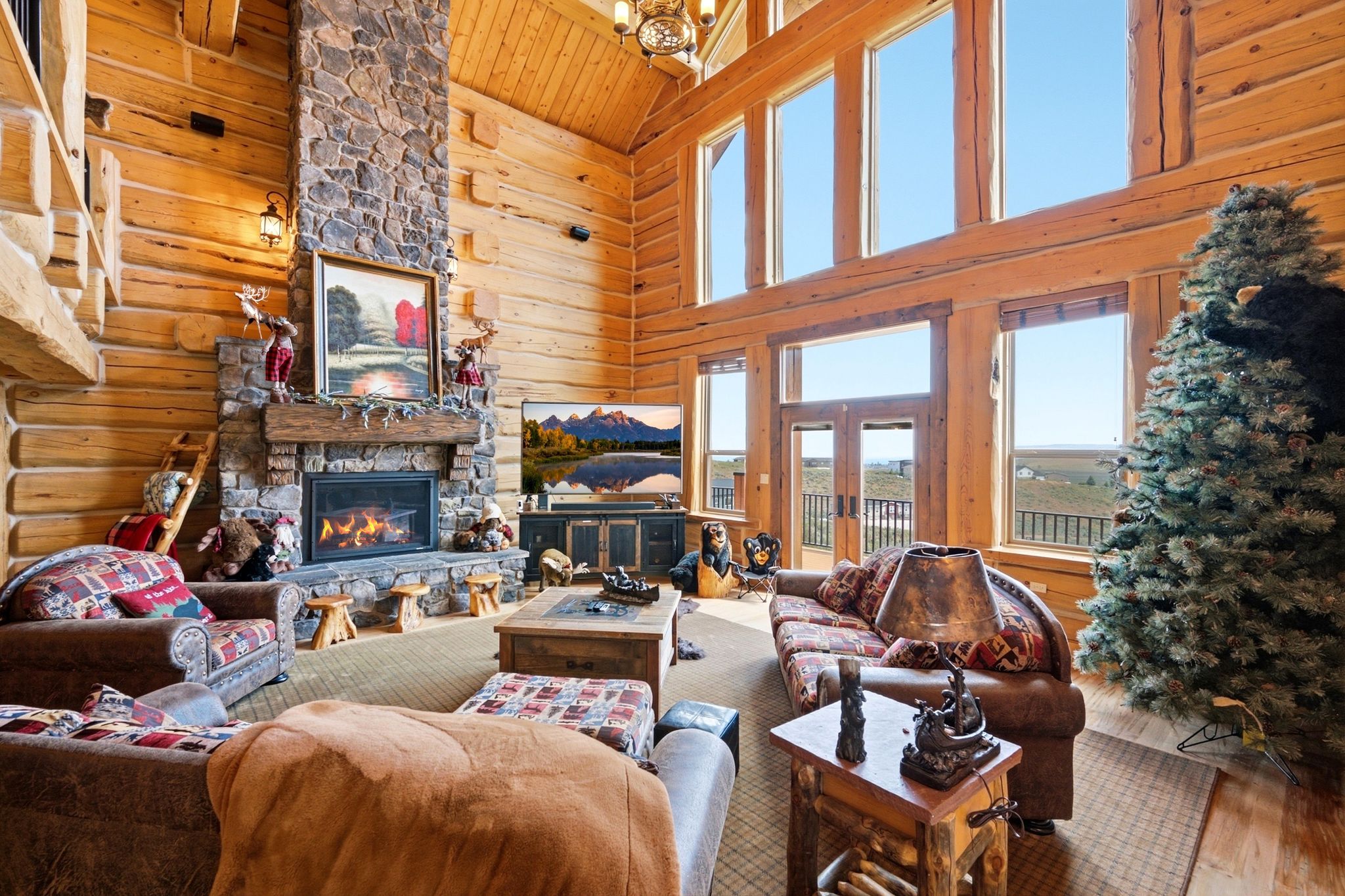 Great room featuring log construction, a floor-to-ceiling stone fireplace, high vaulted ceilings, and extensive window walls