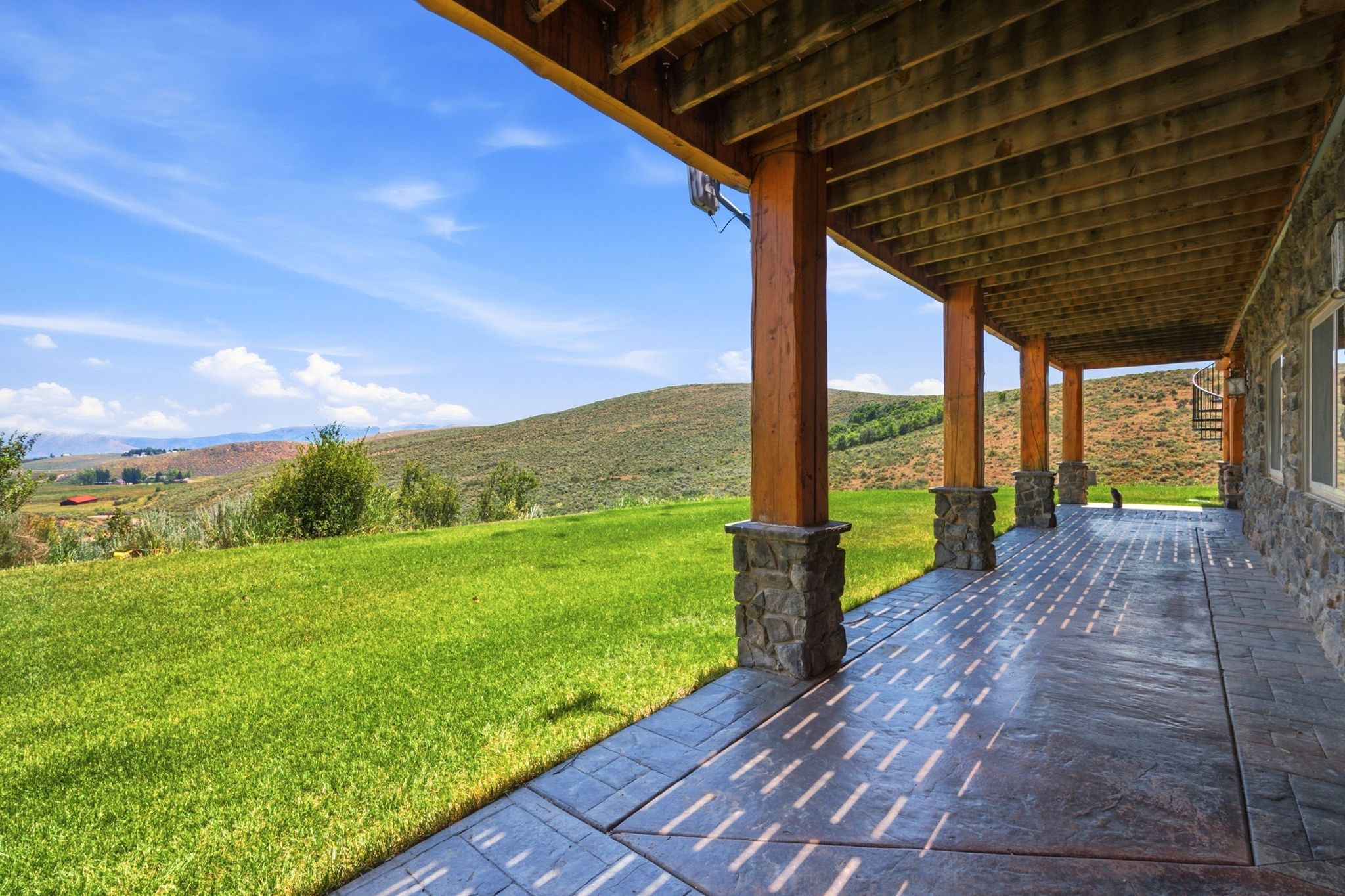 Expansive covered patio featuring stamped concrete flooring and stone-clad support pillars