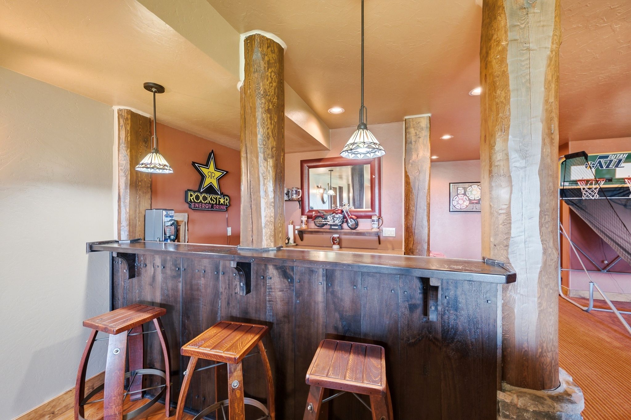Custom bar area featuring a dark wood-finish bar, three bar stools, and two pendant light fixtures