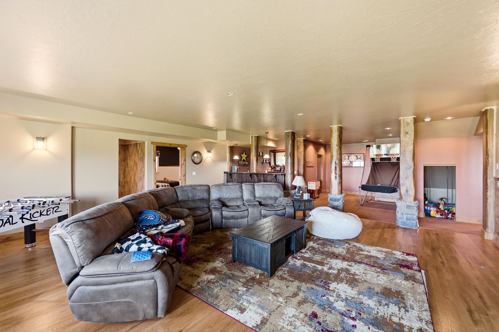 Spacious open-concept recreation room featuring wood-finish flooring, recessed lighting, and several structural columns with stone bases
