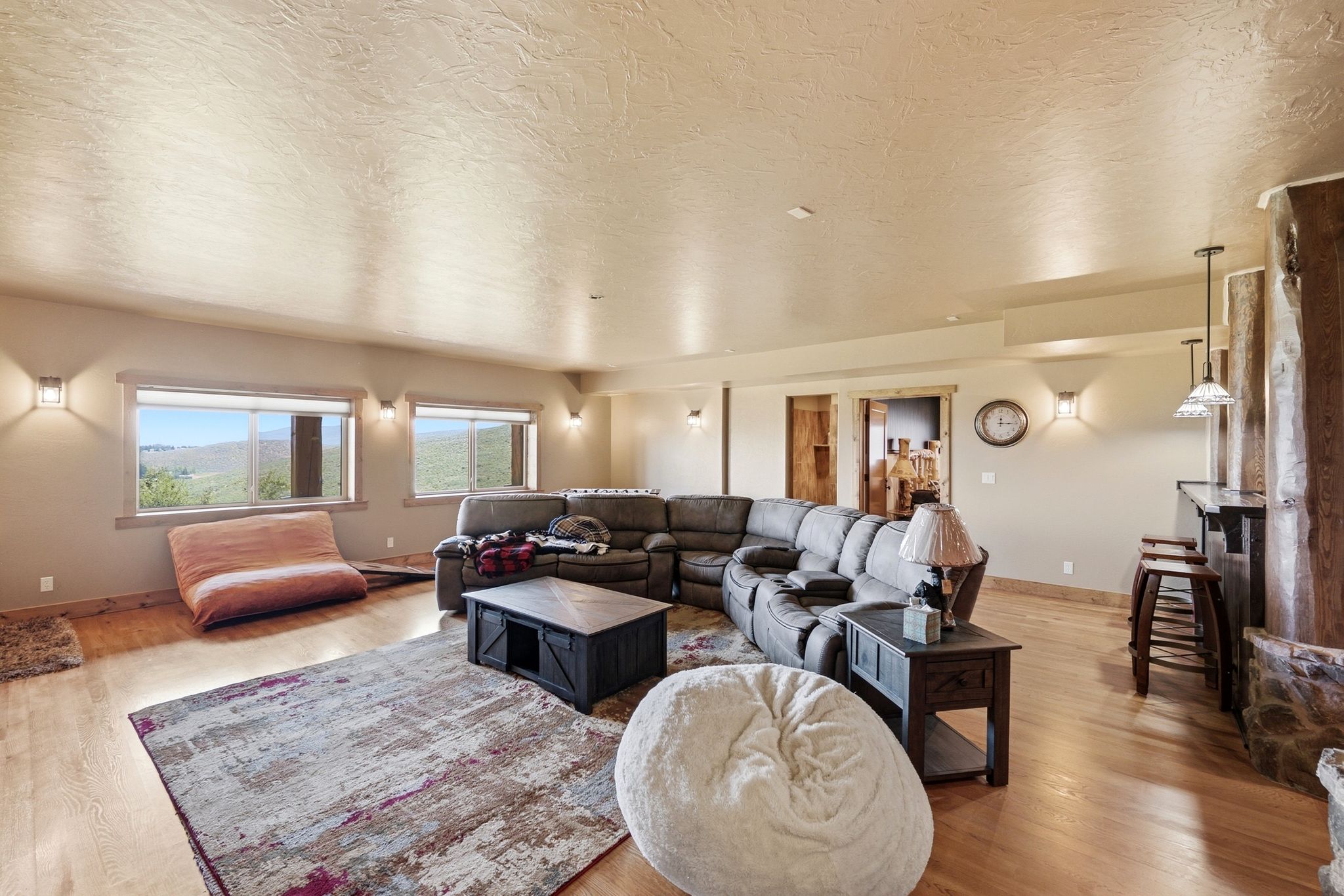 Spacious living area featuring wood-finish flooring, multiple windows offering landscape views, and a dedicated bar area with pendant lighting