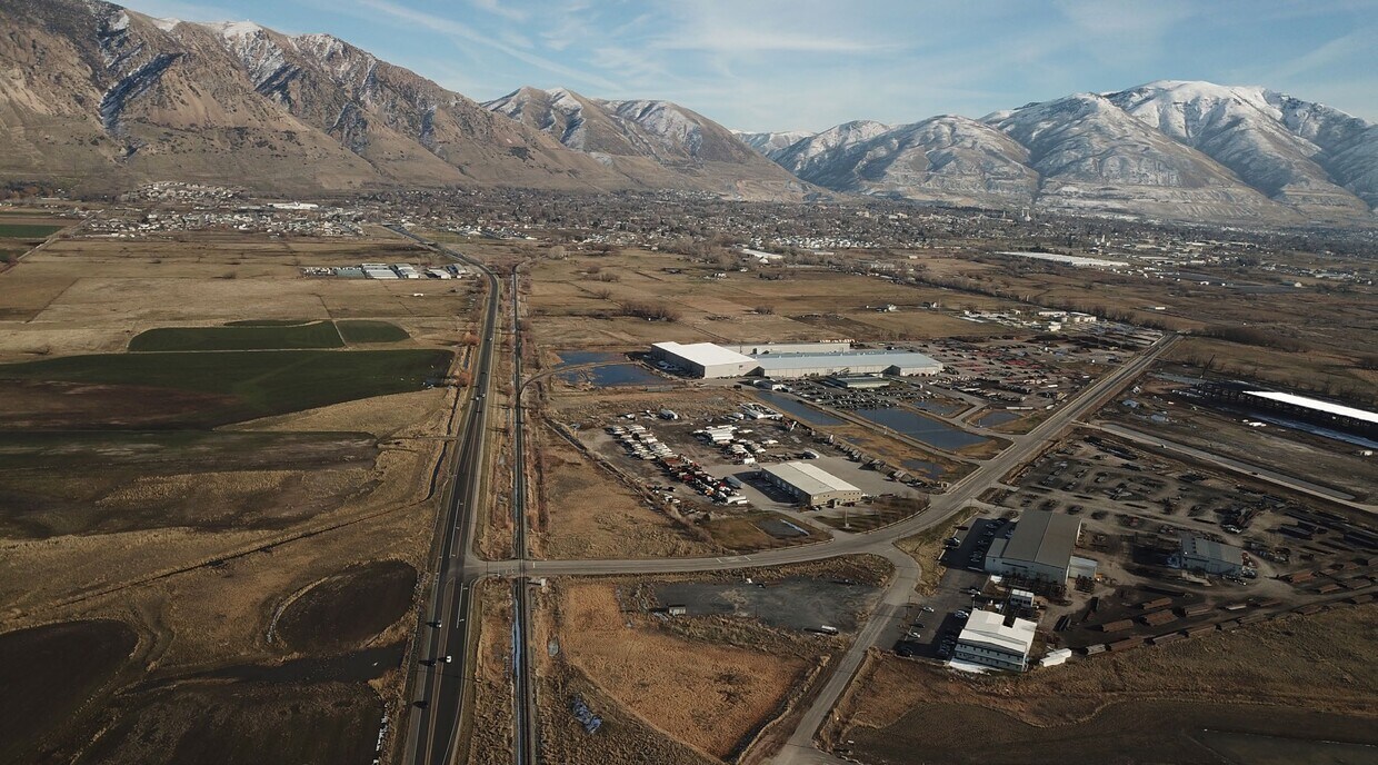 Expansive aerial landscape featuring a highway, commercial structures, and a residential area with snow-capped mountains in the background
