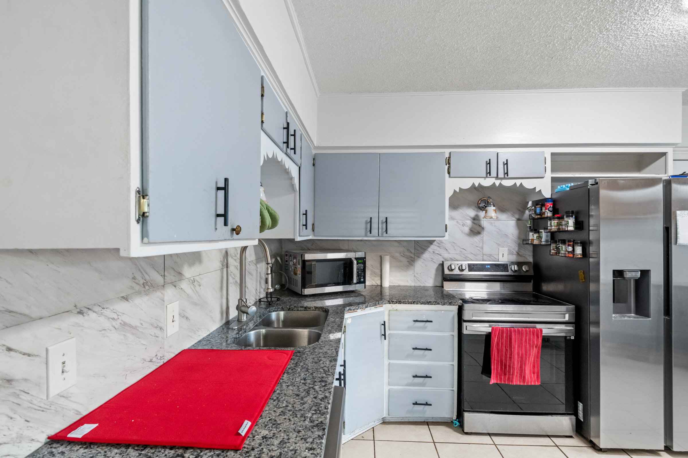 Kitchen featuring light blue upper cabinetry with black hardware, stone-look countertops, stainless steel double basin sink, and a large stainless steel refrigerator