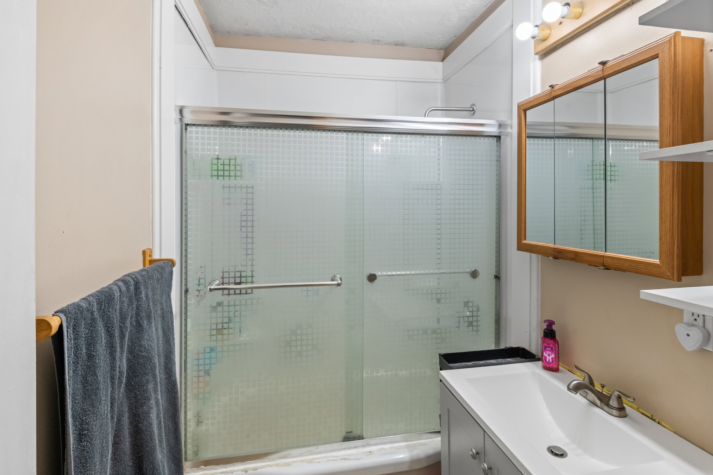 Bathroom featuring a shower with patterned frosted glass sliding doors, a vanity with an integrated white sink, brushed nickel faucet, and a wall-mounted mirrored medicine cabinet with wood-finish trim