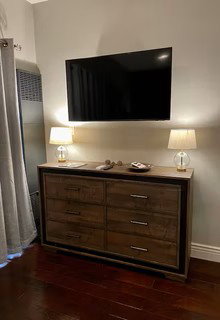 Wall-mounted television above a six-drawer dresser with metal hardware and a wood-finish surface