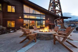 Outdoor patio featuring a built-in stone fire pit, extensive concrete hardscaping, and large glass sliding doors providing access to the interior