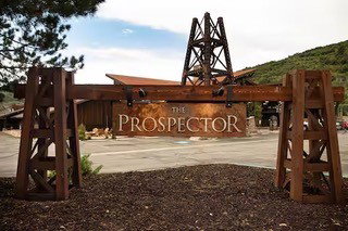 "The Prospector" sign crafted from wood-finish materials and weathered metal, featuring a decorative mining derrick structure