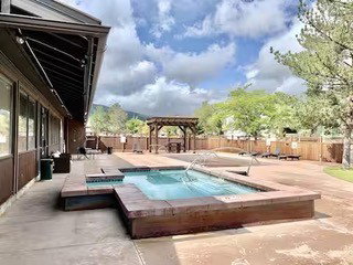 Outdoor aquatic area featuring a swimming pool with an integrated hot tub, extensive concrete patio, and a wooden pergola structure