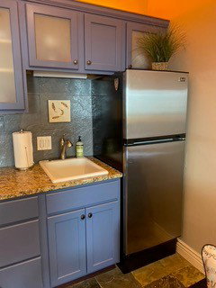 Compact kitchen area featuring a stainless steel refrigerator, blue-painted cabinetry with frosted glass inserts, a single-basin sink, and granite-finish countertops