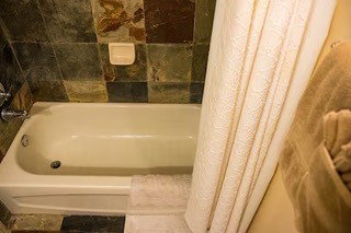Alcove bathtub with a neutral finish, surrounded by variegated stone-finish wall tile and coordinating floor tile