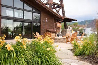 Exterior featuring a large wall of windows, an adjacent sliding glass door, natural wood siding, and a covered patio area with stone pavers