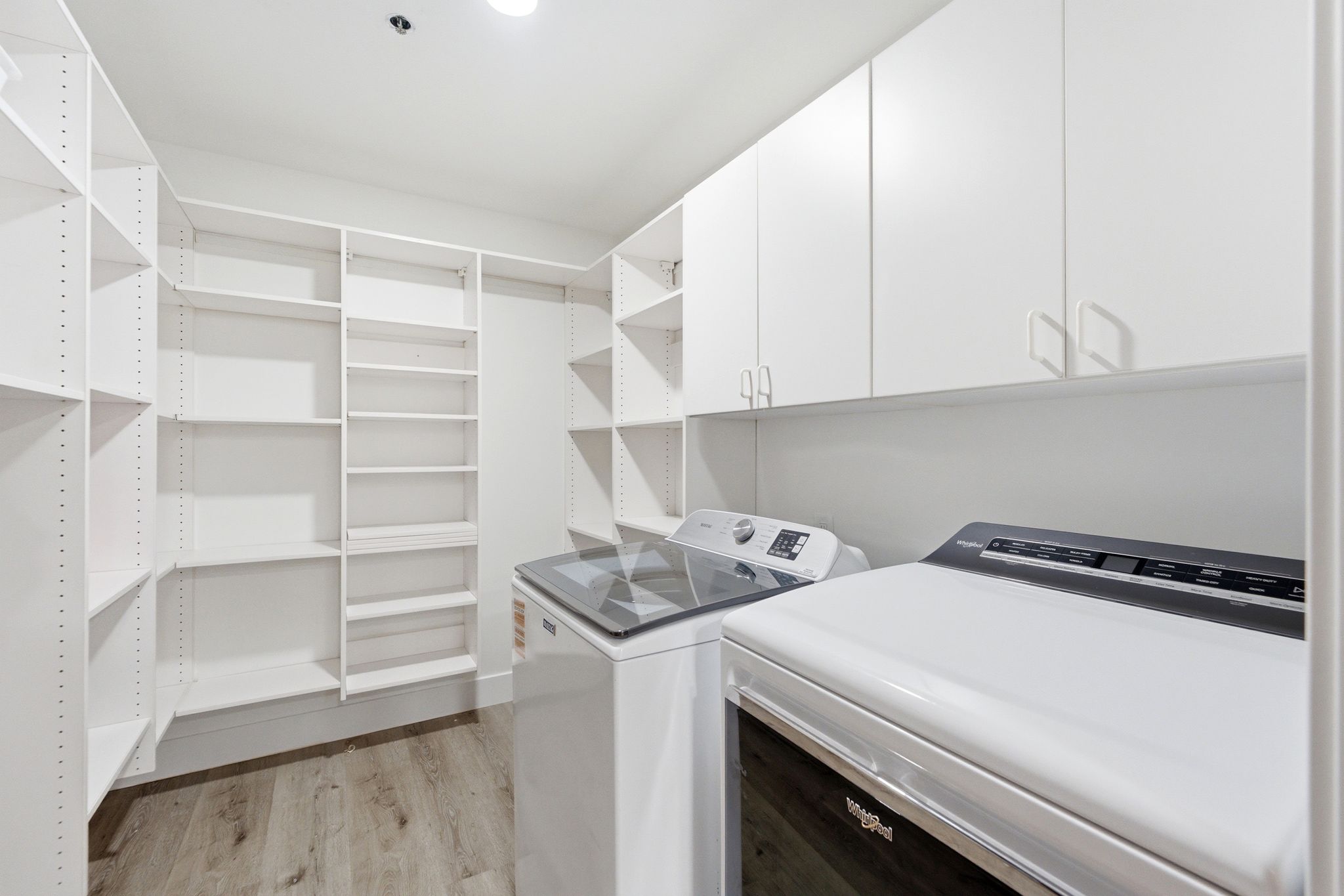 Dedicated laundry area featuring white upper cabinetry and wood-finish flooring