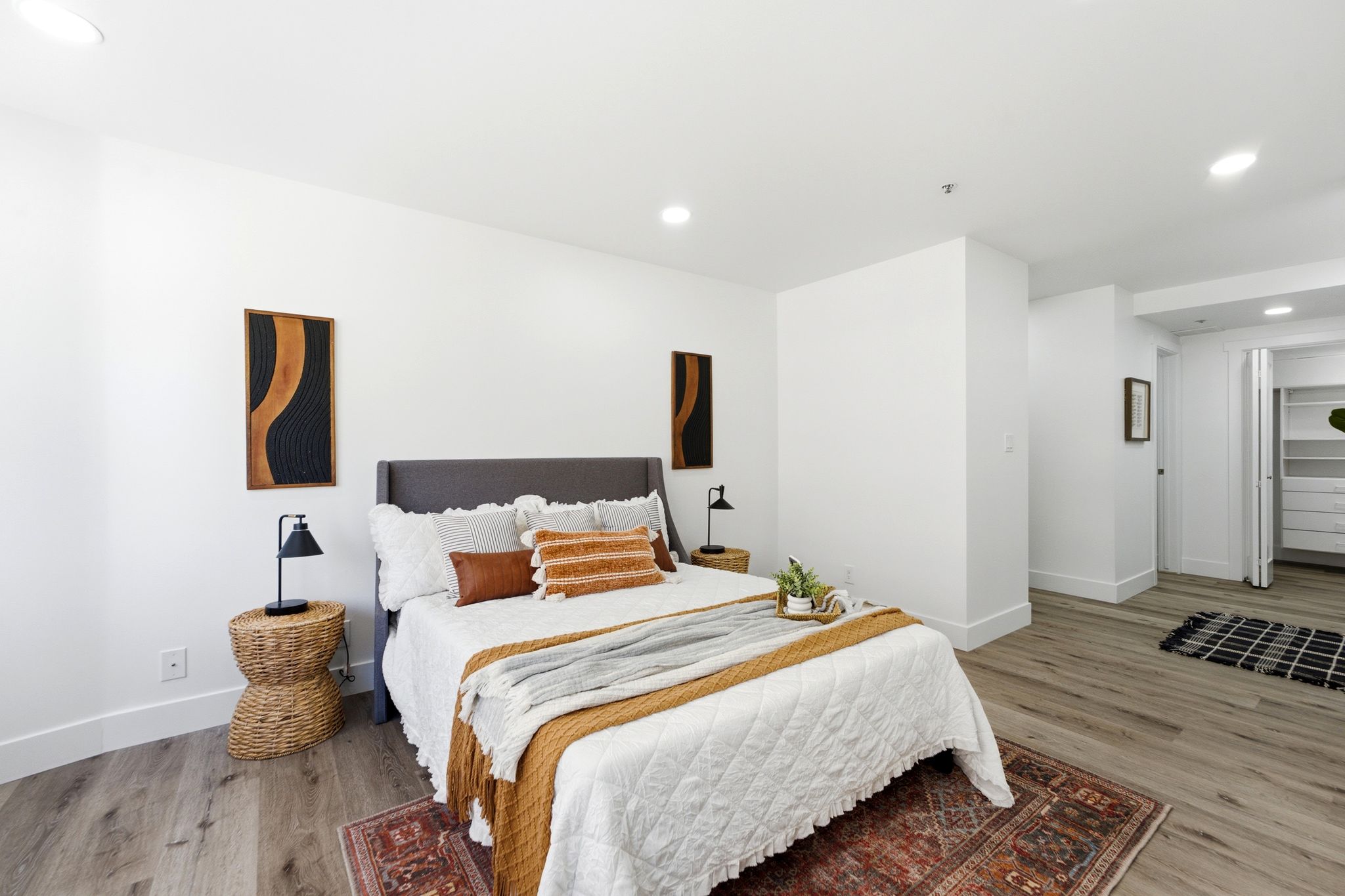 Bright and spacious master bedroom featuring light wood-finish flooring, white walls, recessed lighting, and a walk-in closet with built-in shelving and drawers