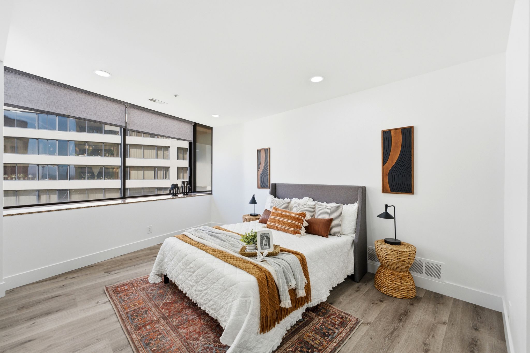 Spacious Master bedroom featuring a wall of windows with roller shades, wood-finish flooring, recessed lighting, and crisp white walls