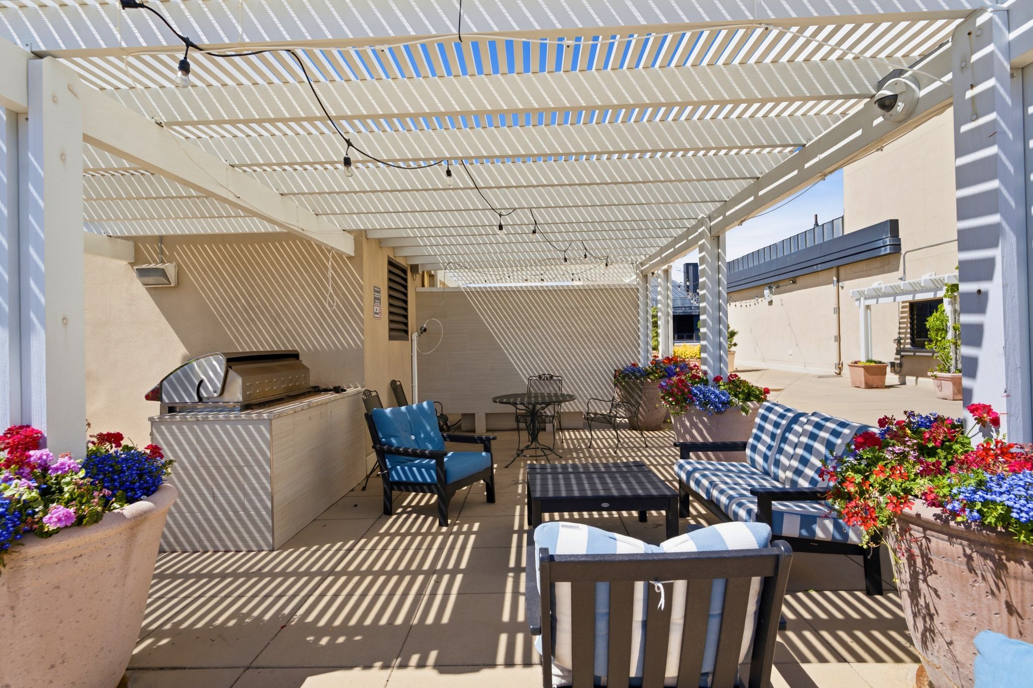 Expansive outdoor patio featuring a white slatted pergola, integrated string lighting, and built-in barbecue station