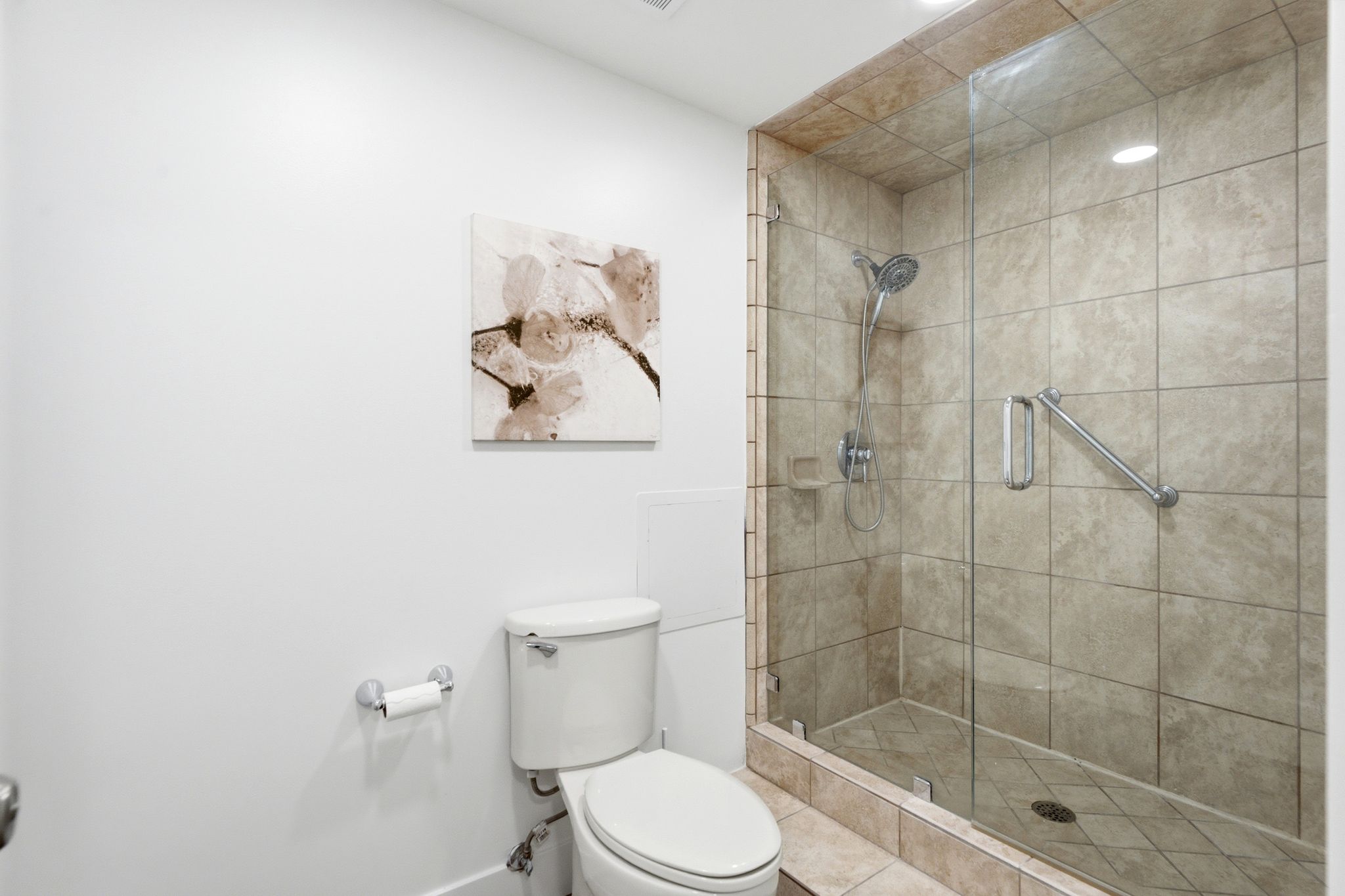 Glass-enclosed master shower with tiled walls and floor, featuring a multi-function showerhead and grab bar