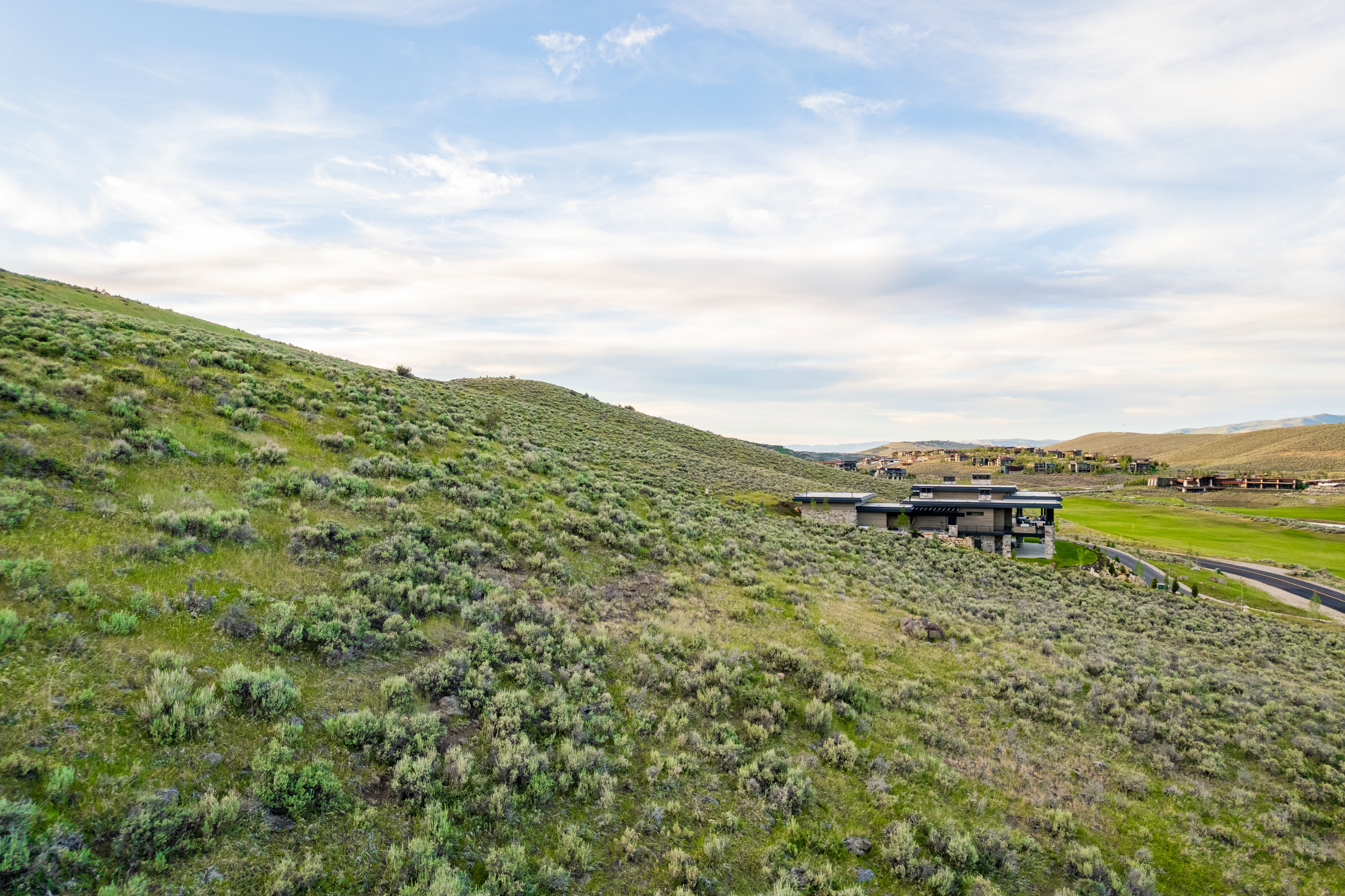 Modern residence featuring stone and dark siding, set into a natural hillside with expansive green spaces