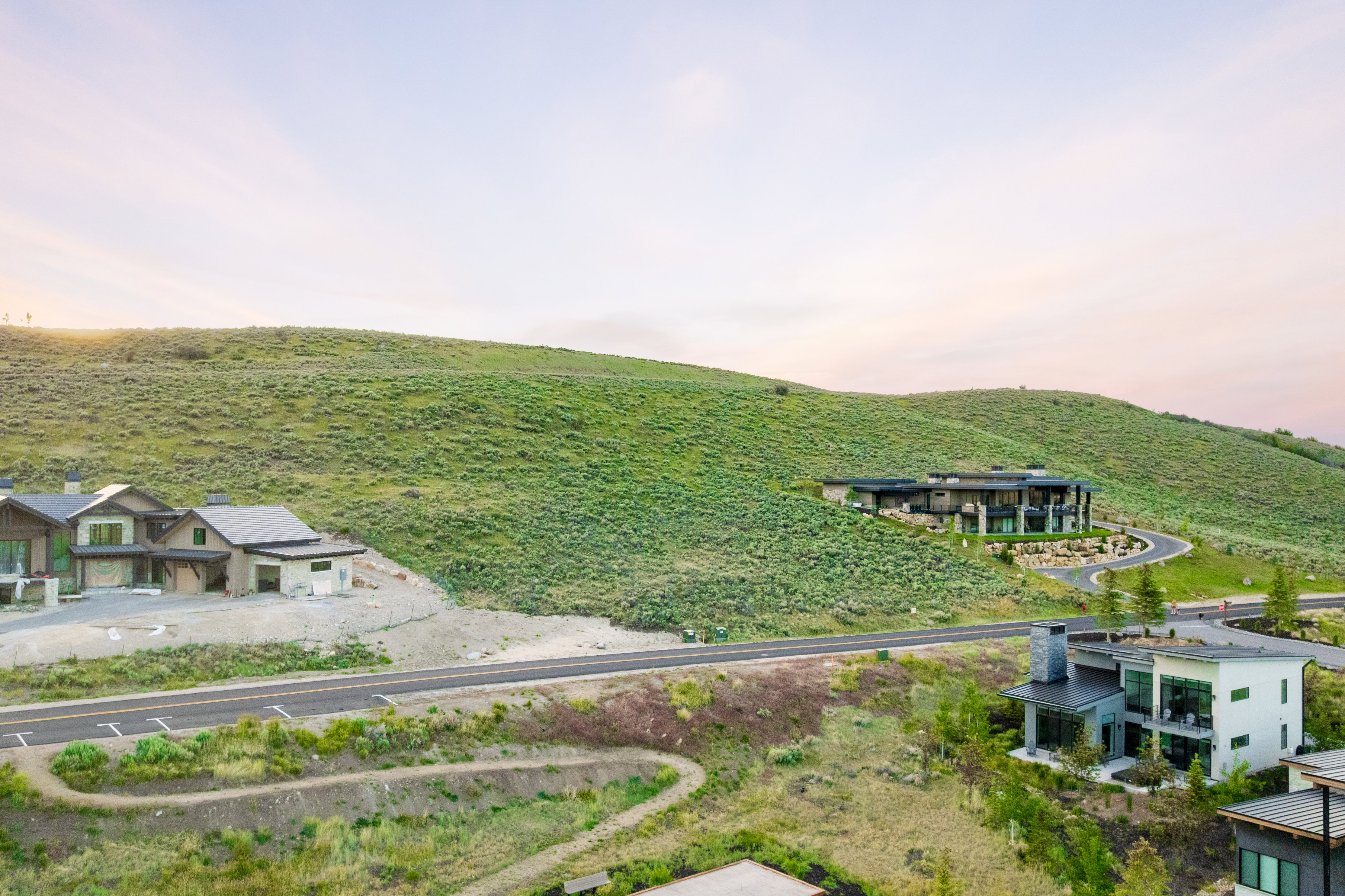 Hillside residence featuring contemporary architecture with expansive windows, multiple outdoor living spaces, and a winding driveway