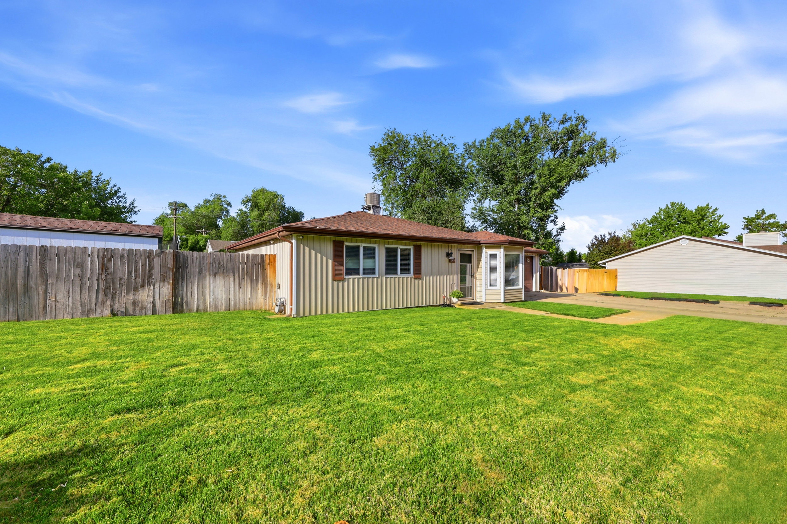 Spacious front lawn with a single-story residence featuring vertical siding and a bay window