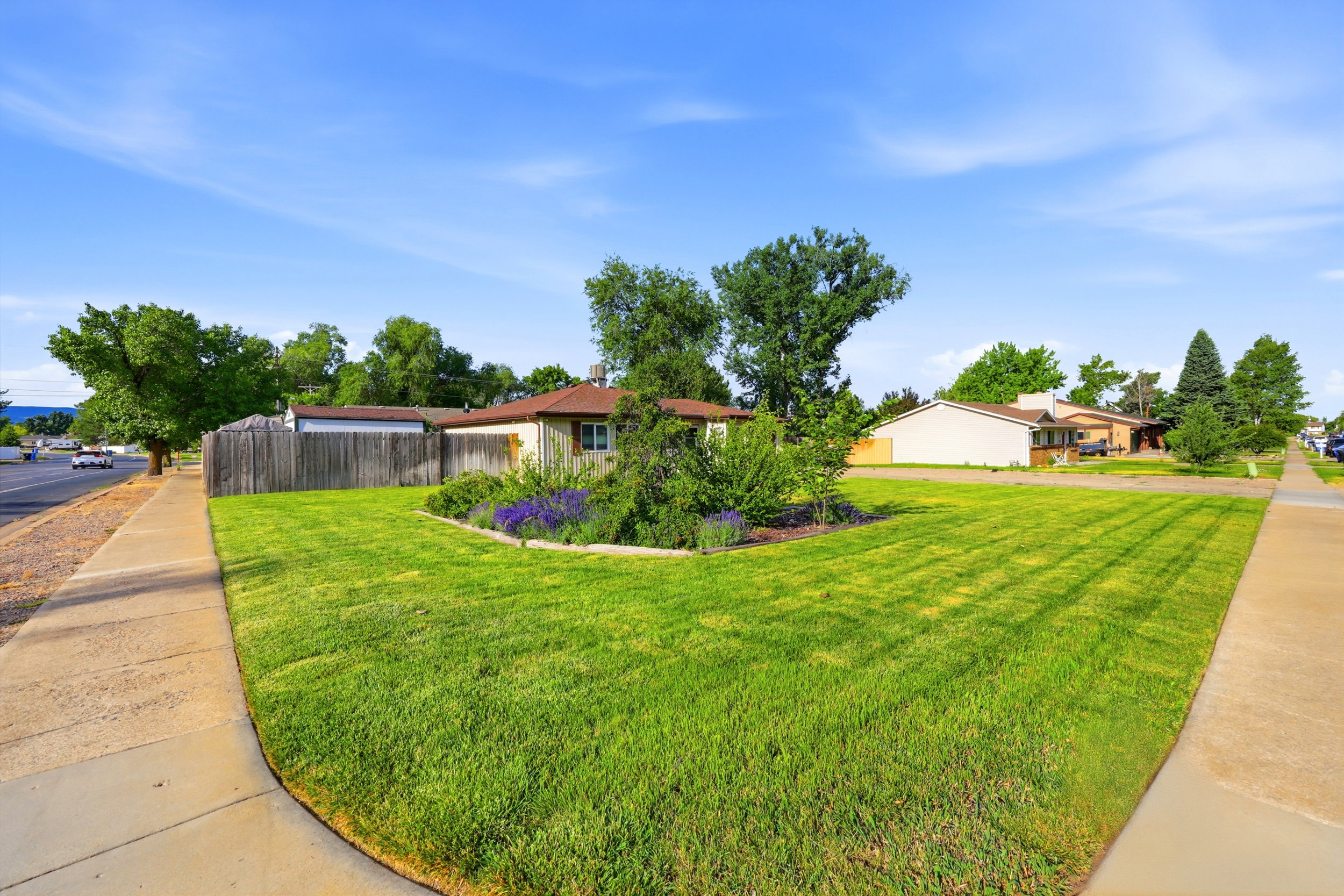 Manicured front lawn with a curved planting bed featuring shrubs and purple flowering plants