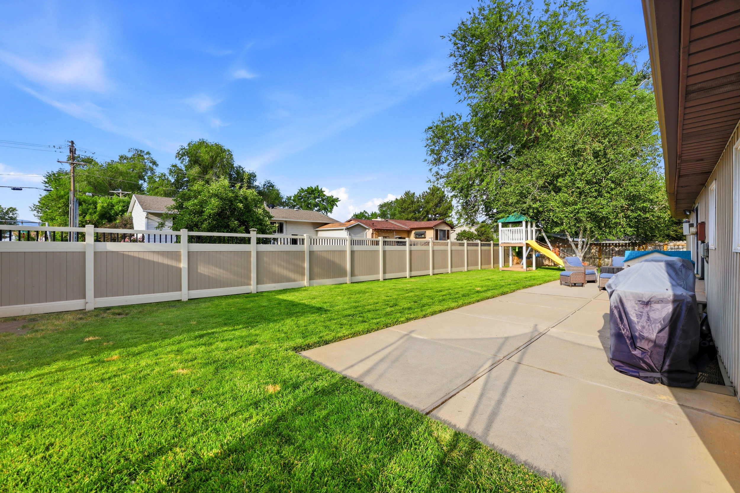 Expansive backyard featuring a concrete patio, a lush green lawn, and a two-tone privacy fence