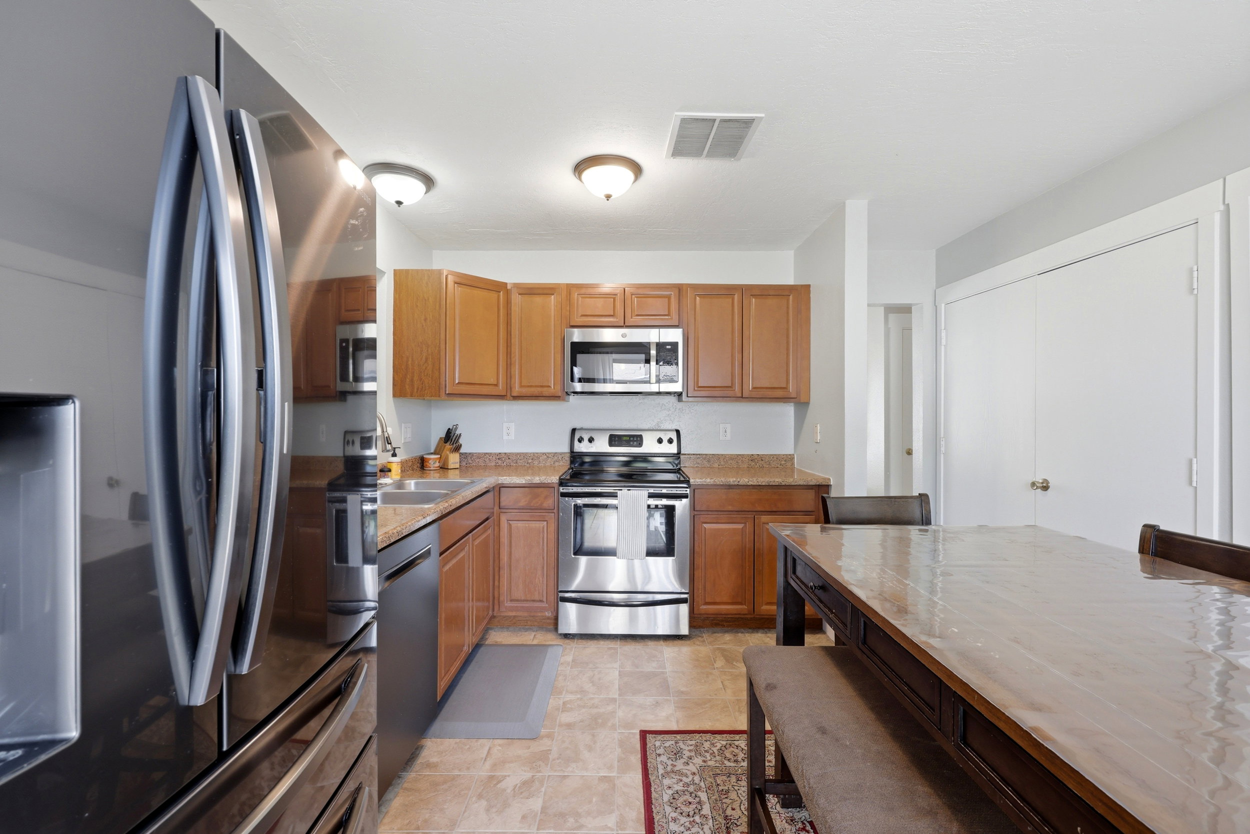 Kitchen featuring stainless steel appliances, wood cabinetry, stone countertops, and tile flooring