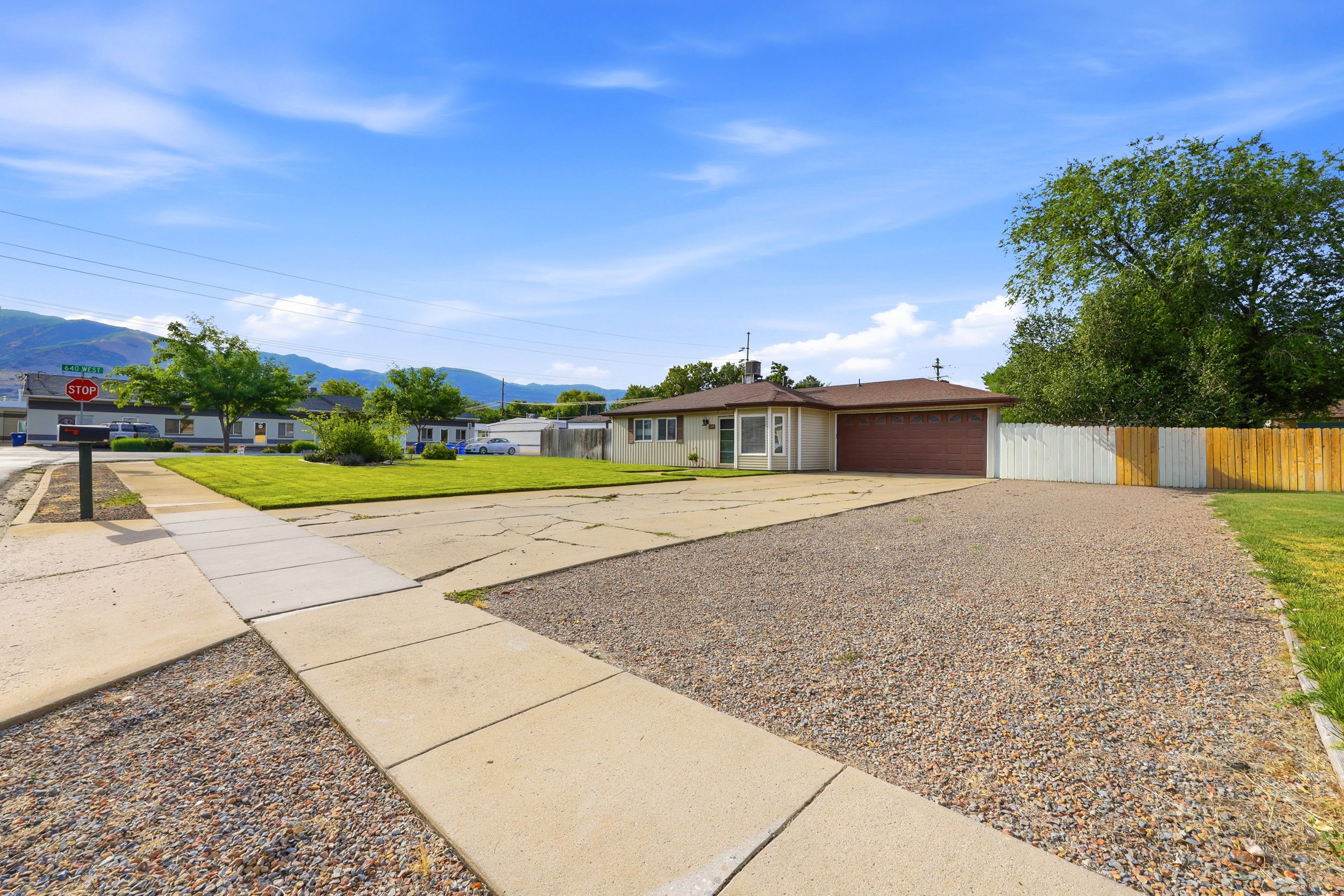 Single-story residence featuring a two-car garage with a brown door, front lawn, and a gravel driveway