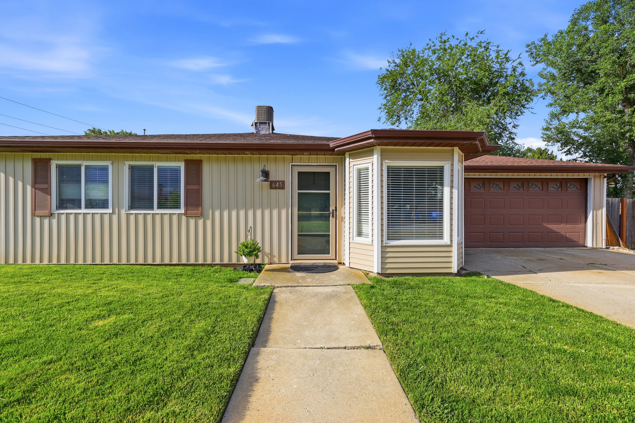 Ranch-style exterior featuring vertical siding, bay window with blinds, attached two-car garage, and concrete walkway