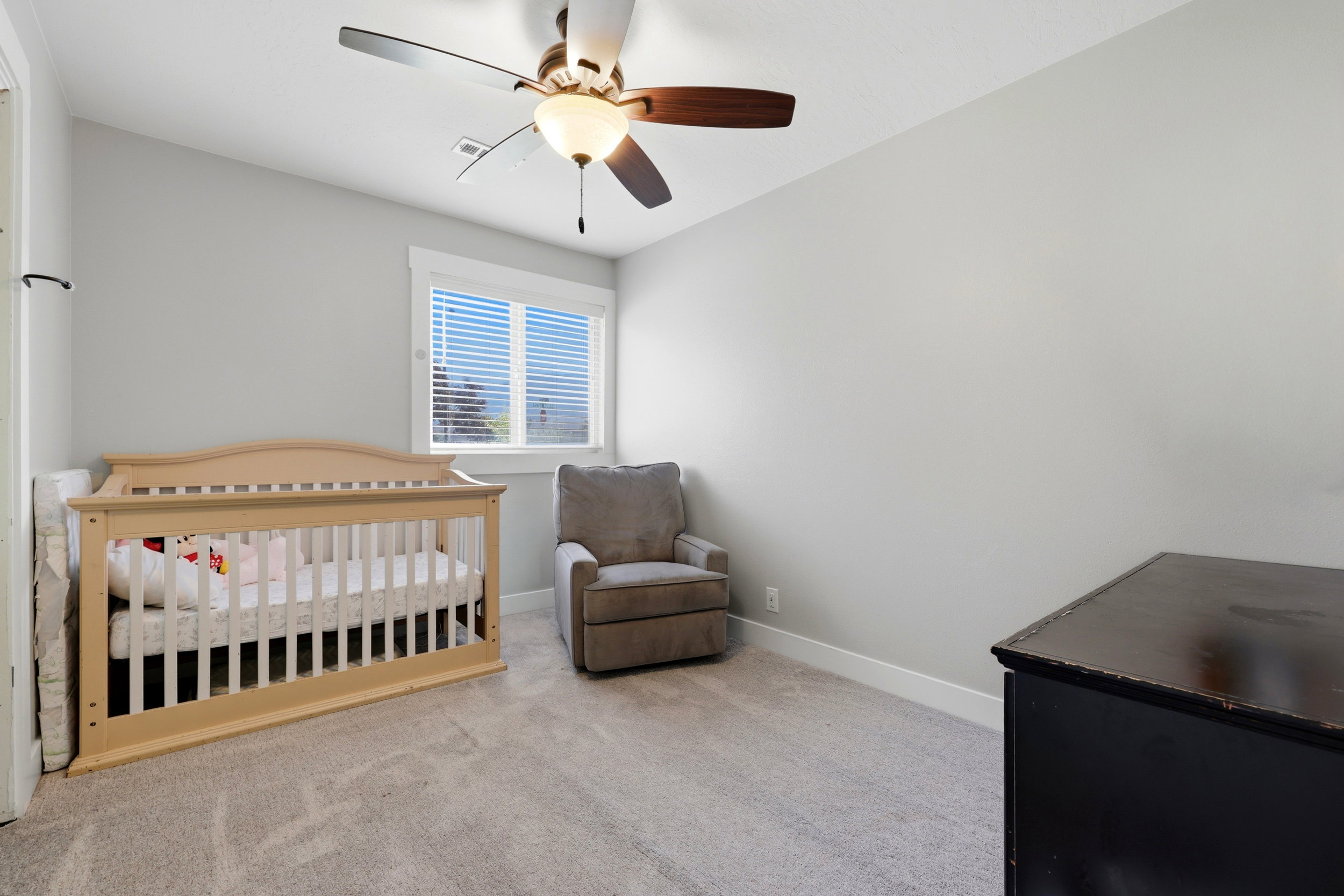 Bright room featuring a window with horizontal blinds, neutral-toned carpeting, light gray wall paint, and a ceiling fan with integrated lighting