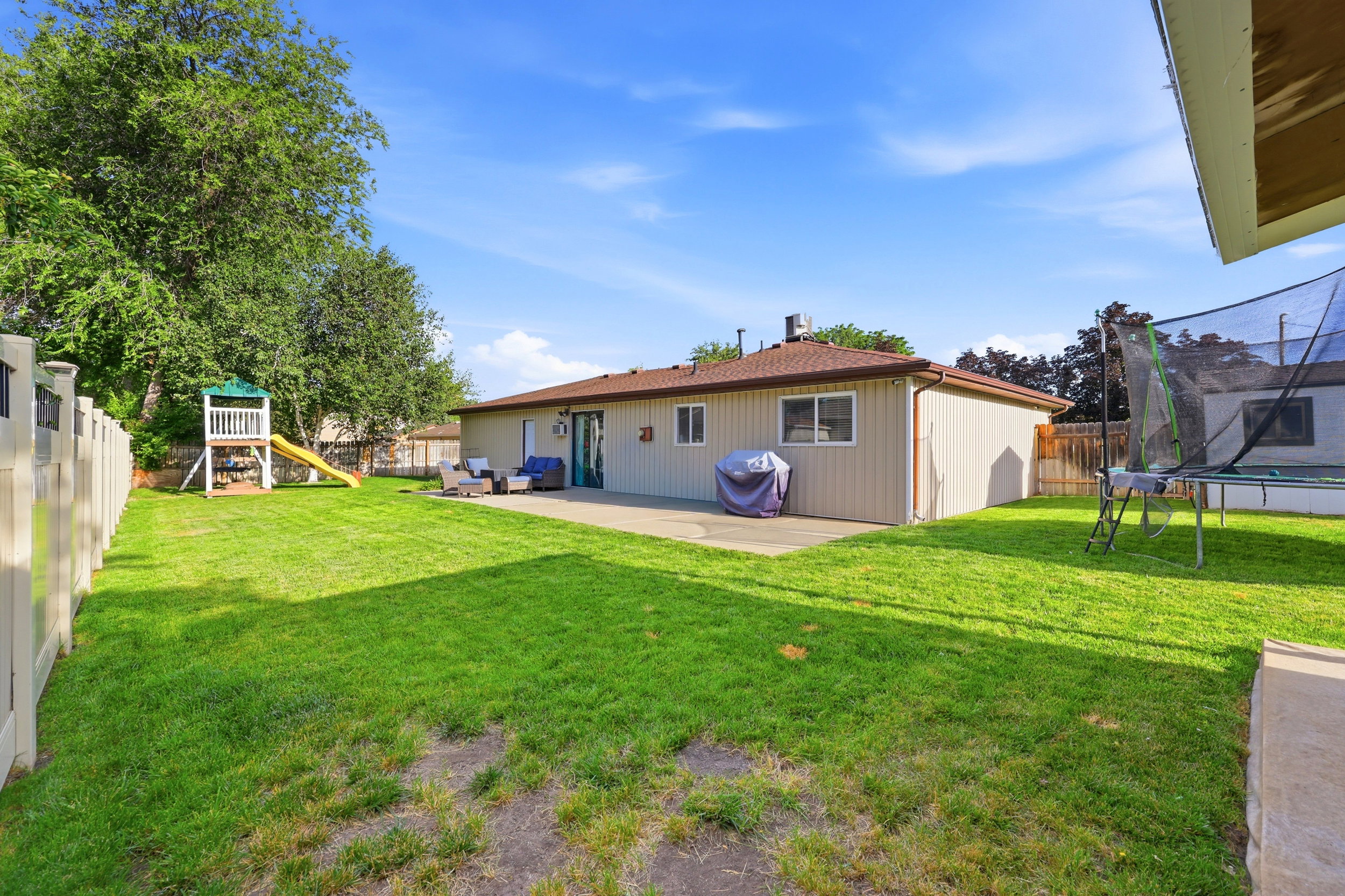 Expansive backyard featuring a large green lawn, concrete patio, and privacy fencing