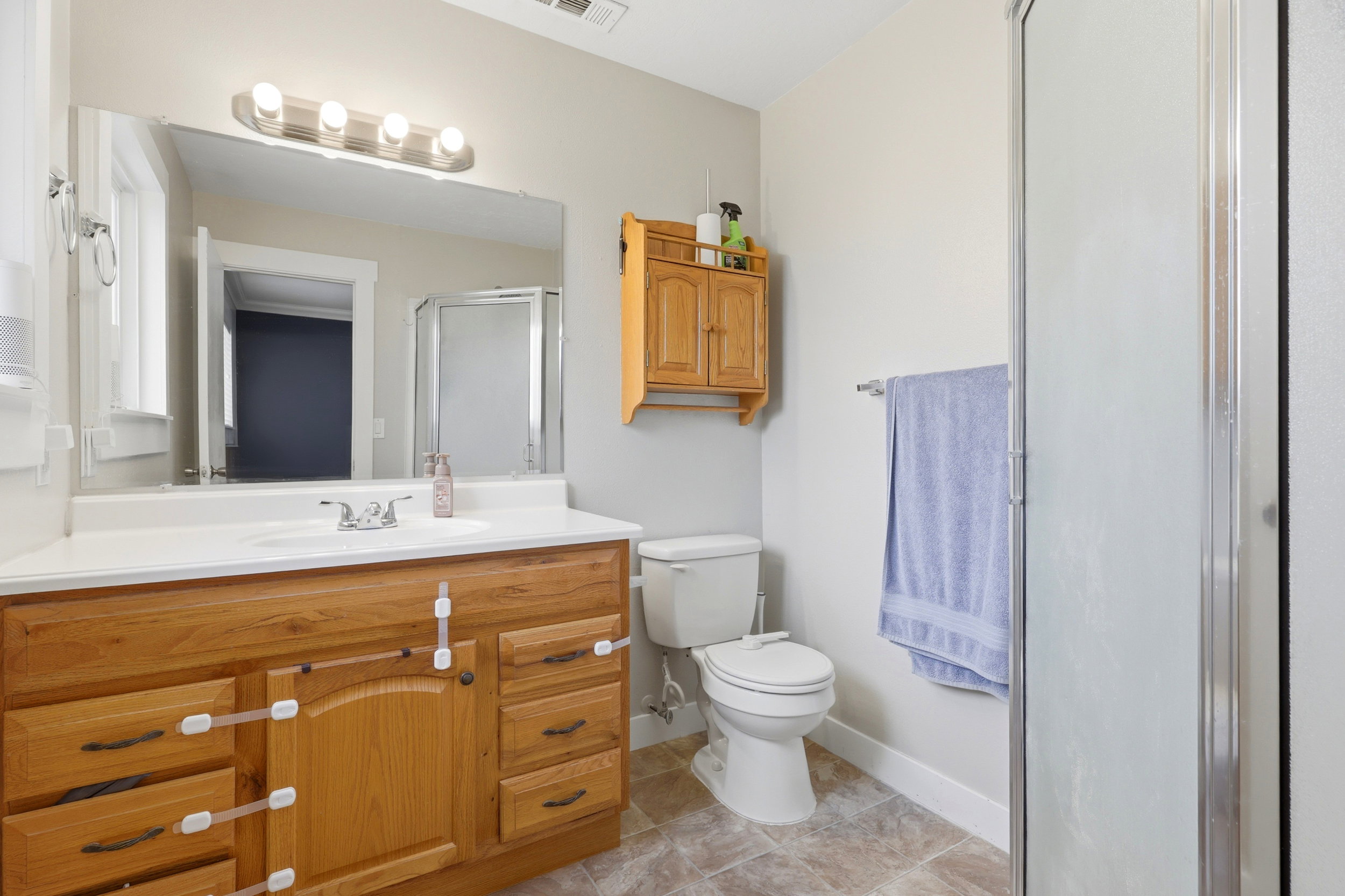 Bathroom featuring a wood-finish vanity with a built-in sink, a full-width mirror, and a standing shower with a frosted glass door