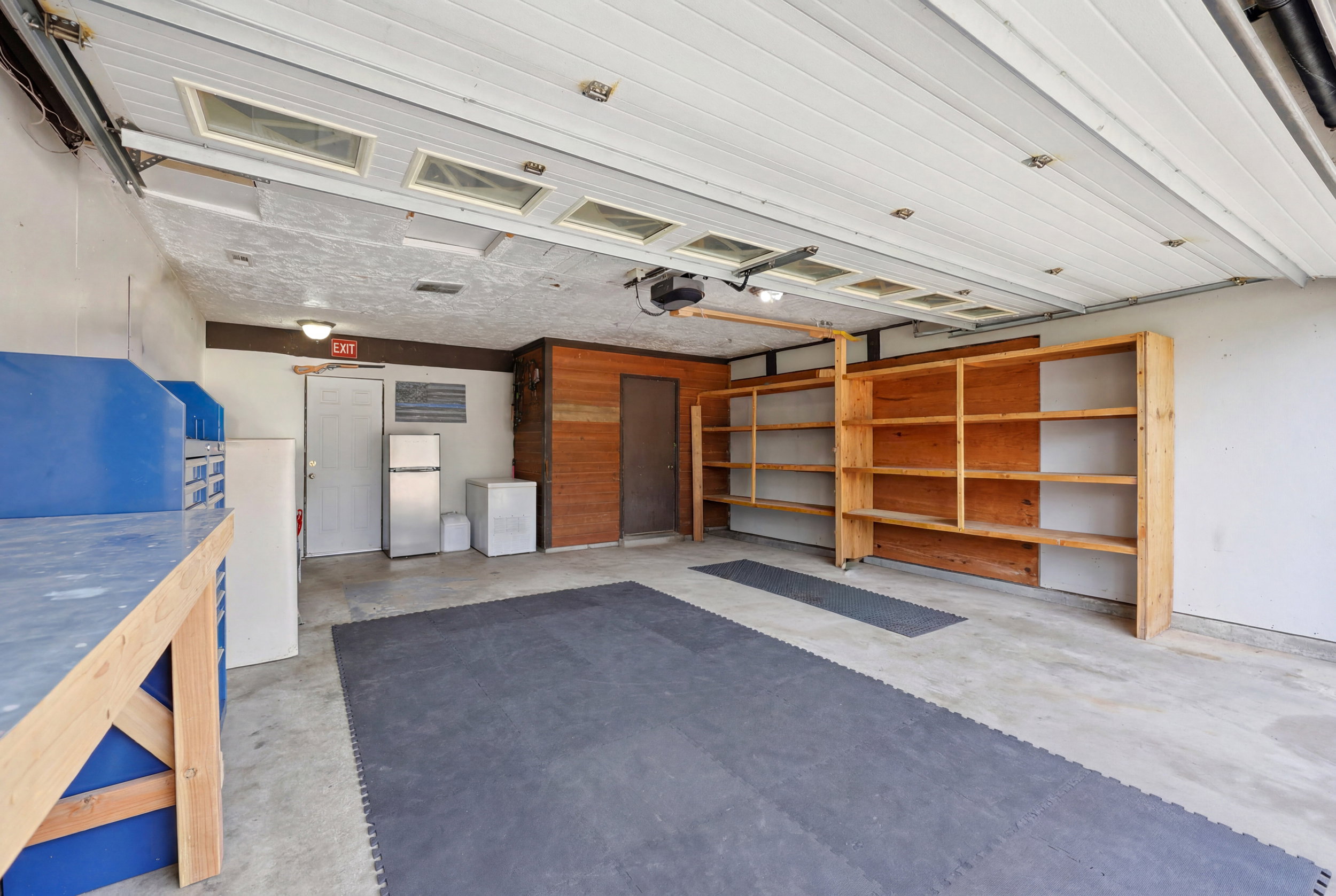 Spacious garage featuring a concrete floor, built-in wooden shelving, a white paneled garage door with integrated windows, and a built-in workbench