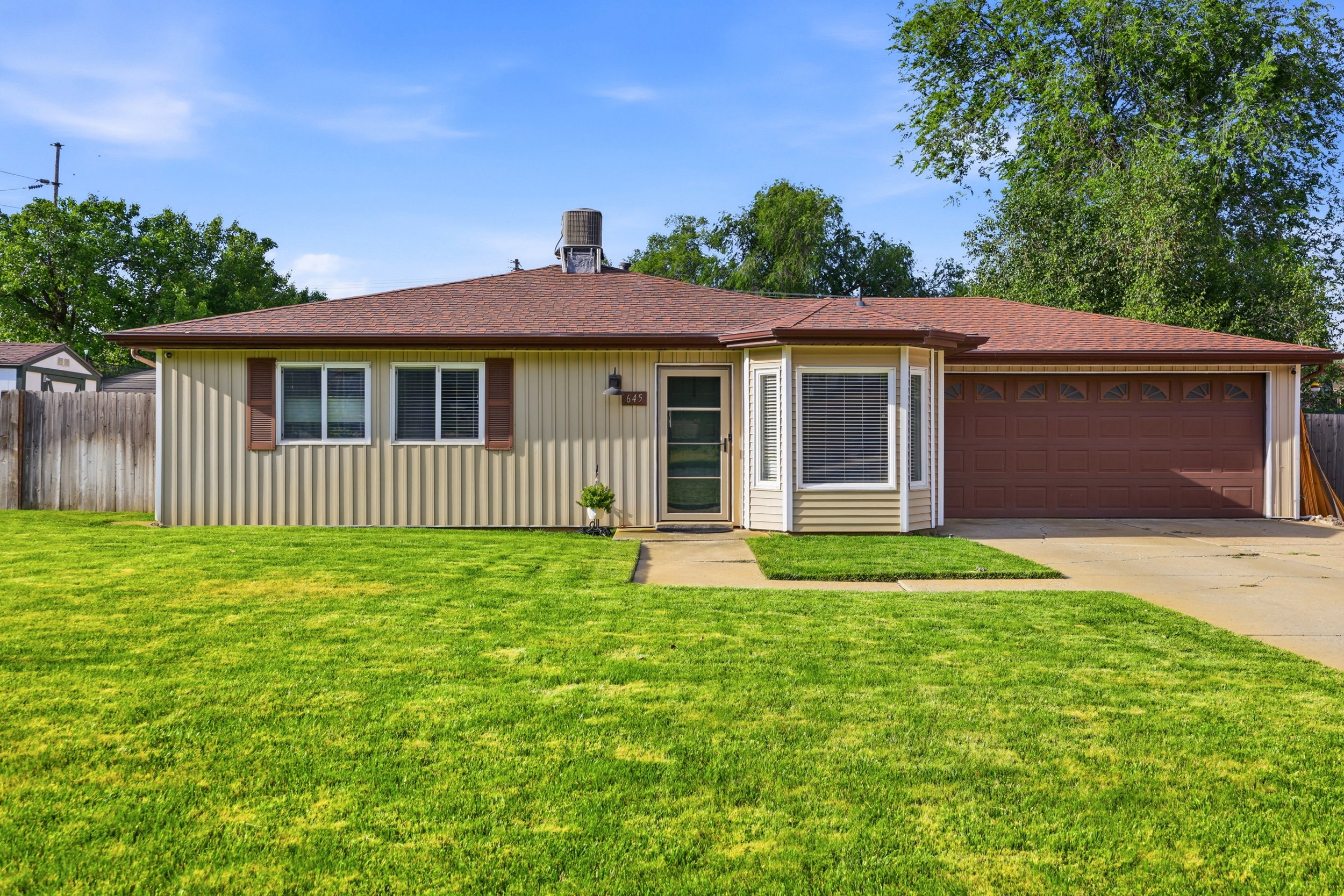 Ranch-style exterior with a brown shingle roof, tan vertical siding, and a two-car attached garage