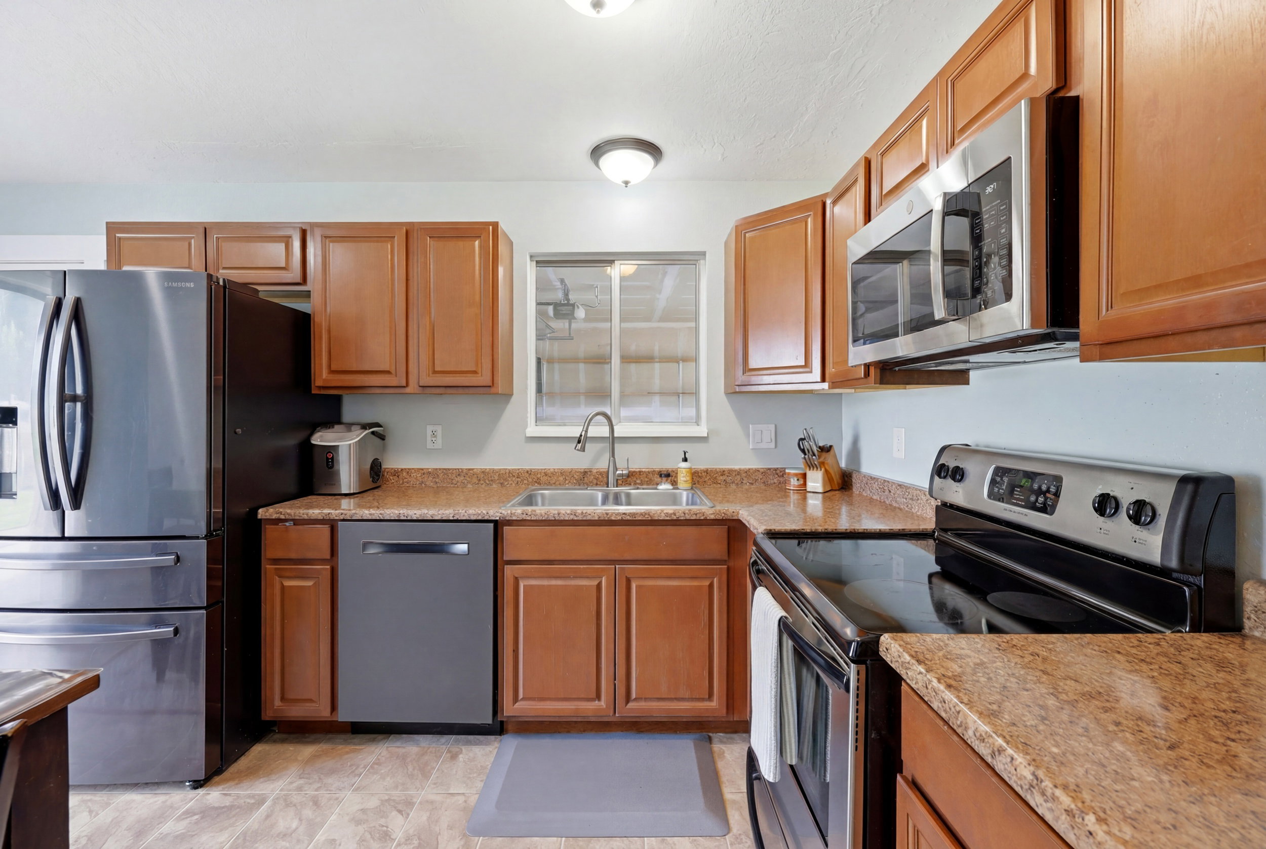 Kitchen featuring wood cabinetry, granite-patterned countertops, and stainless steel appliances including a refrigerator, dishwasher, and over-range microwave