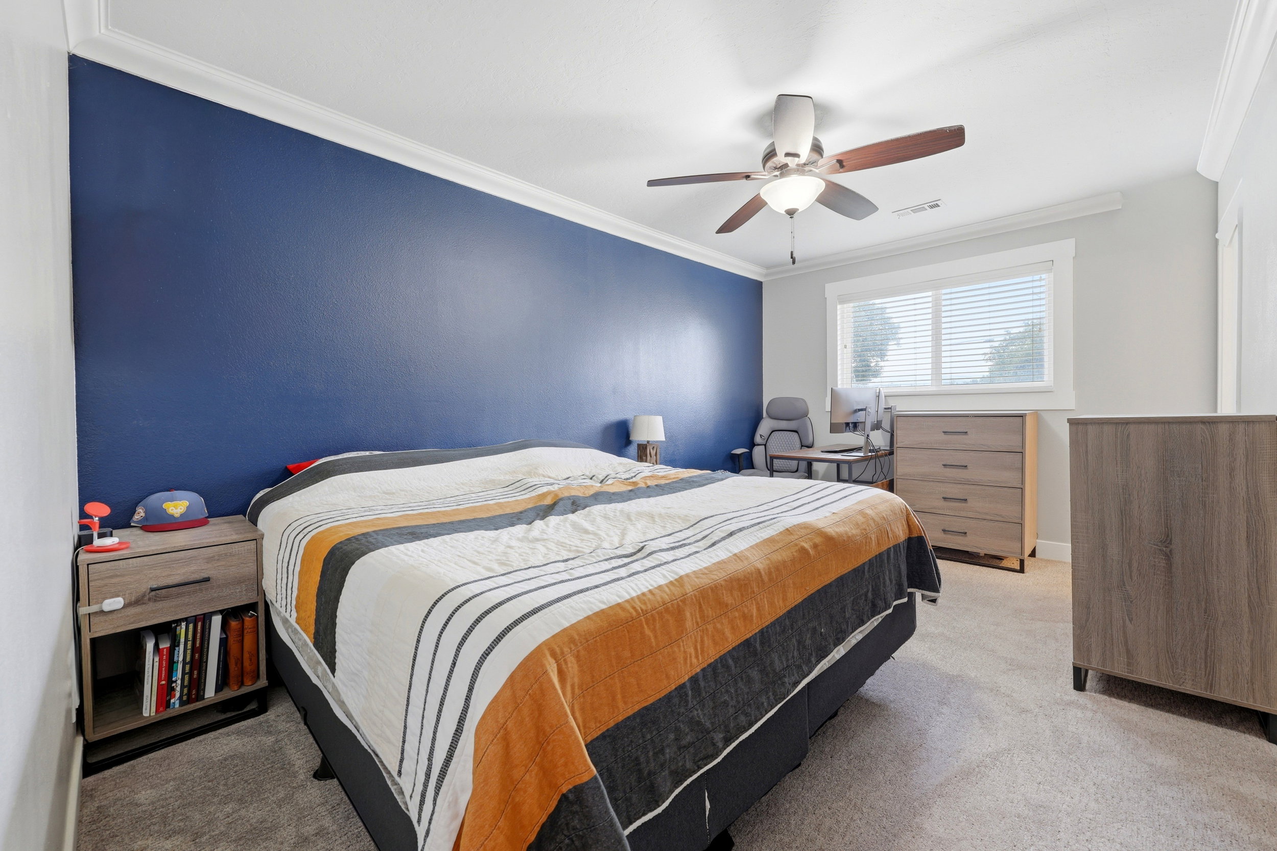 Bedroom featuring a prominent accent wall, ceiling fan with integrated lighting, crown molding, and carpeting