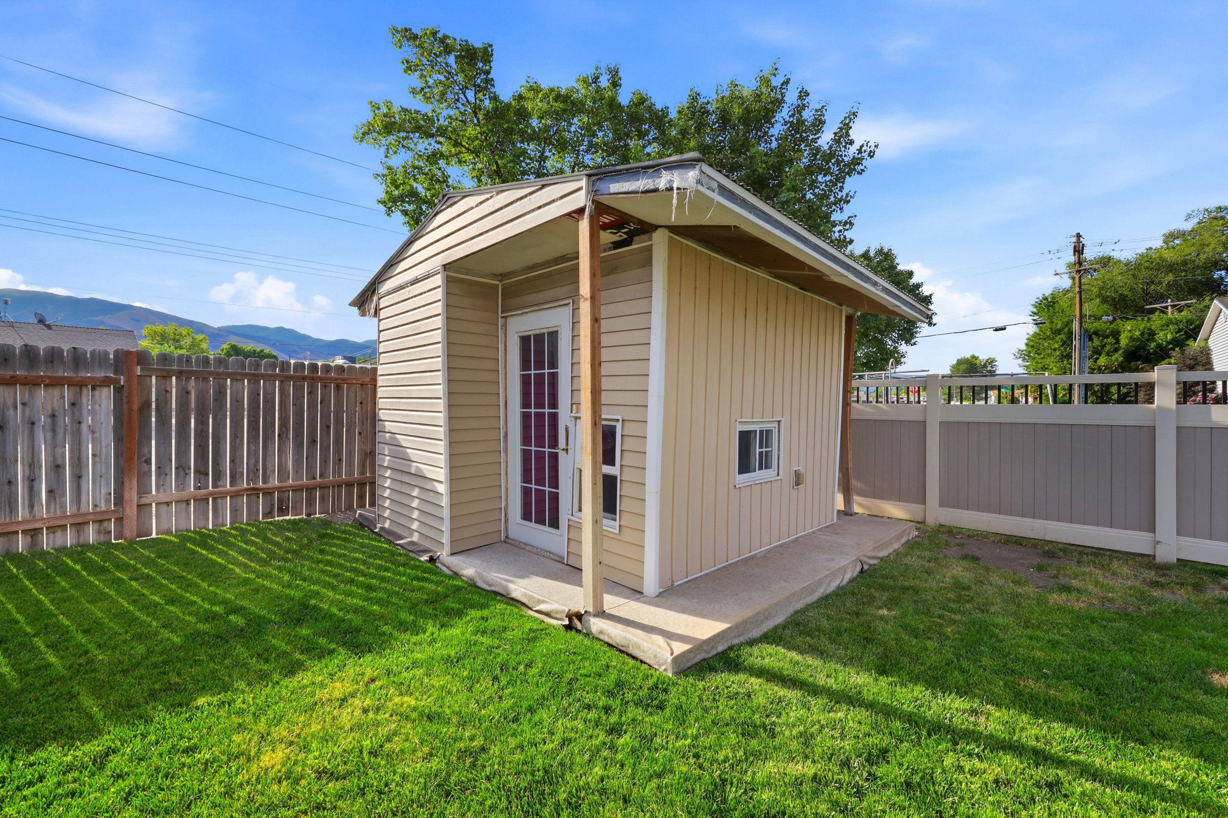 Storage shed with beige siding, a white door, and a small window