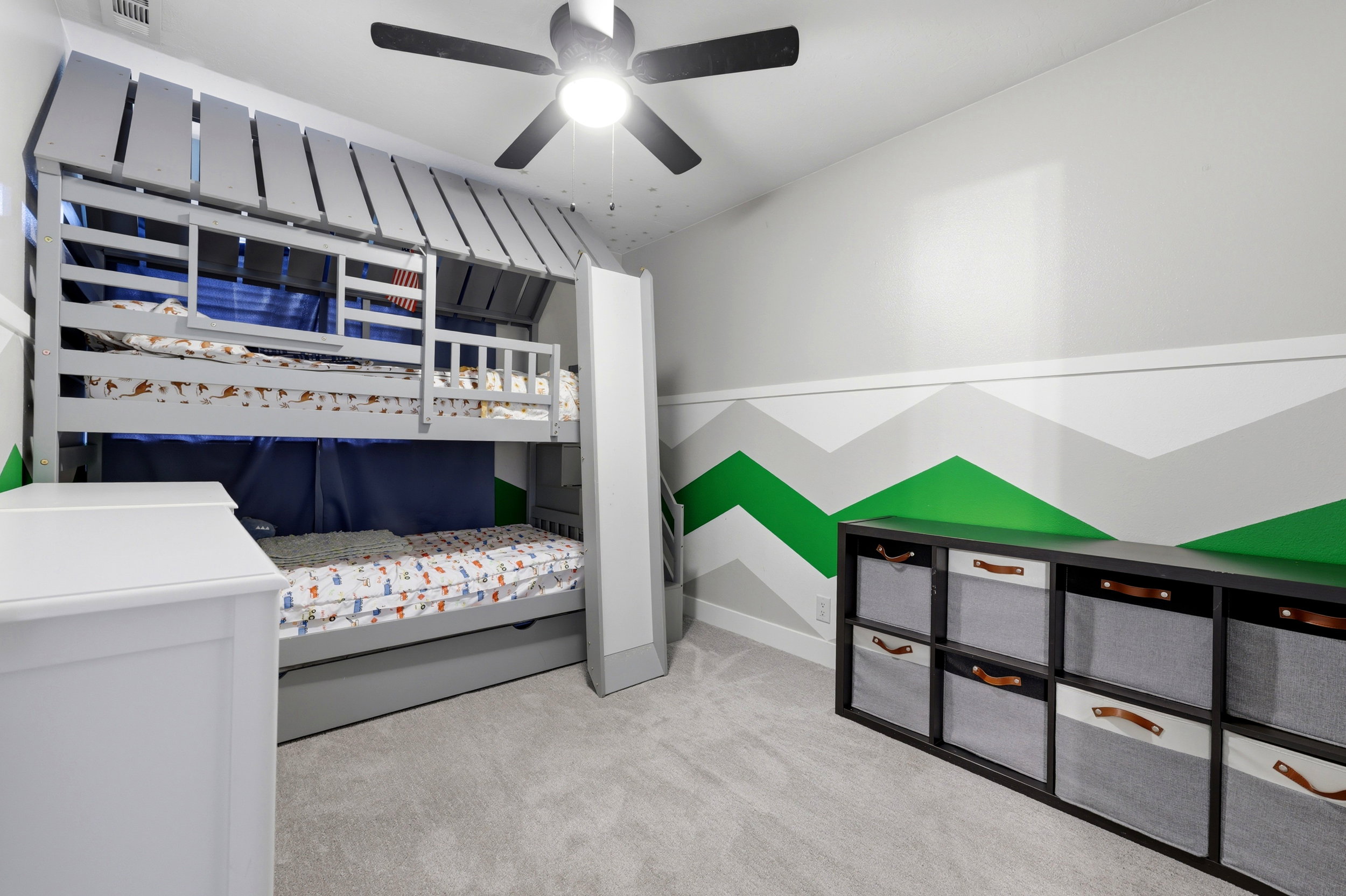 Built-in bunk bed structure with a slide, carpeted flooring, chevron-patterned accent wall, and a ceiling fan with integrated lighting