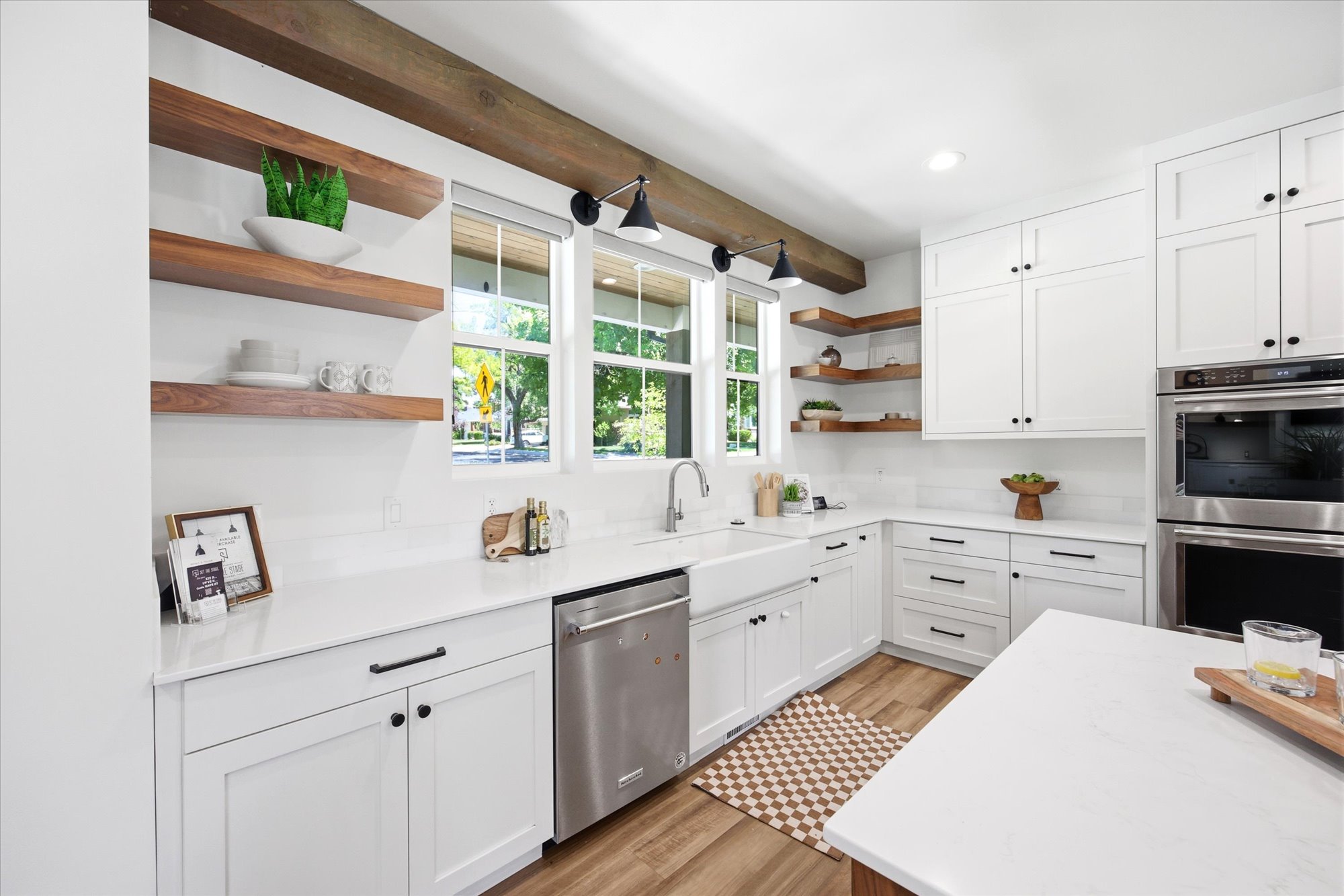 Modern kitchen featuring white cabinetry, quartz countertops, stainless steel appliances, wood-finish flooring, and exposed wood beams