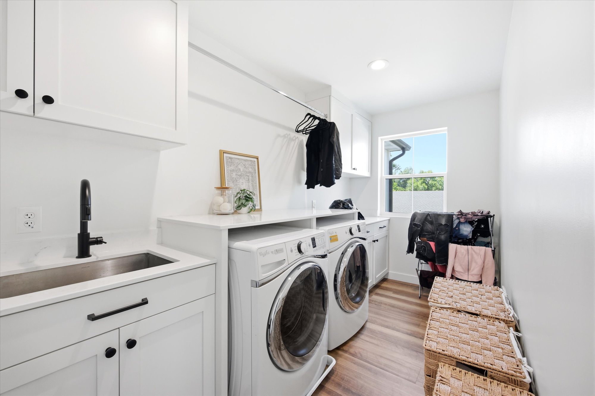 Dedicated utility room featuring wood-finish flooring, white cabinetry with black hardware, a stainless steel sink with a matte black faucet, and ample countertop space